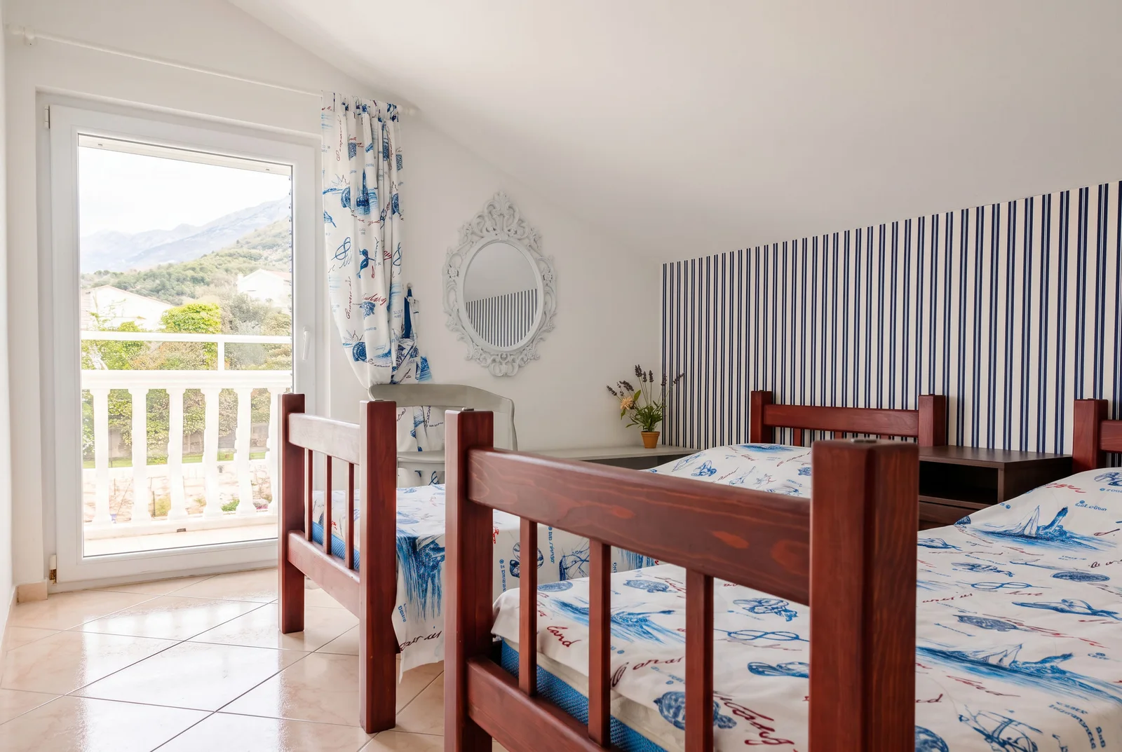 Bedroom with two wooden beds, striped wallpaper, and a balcony door overlooking mountains.