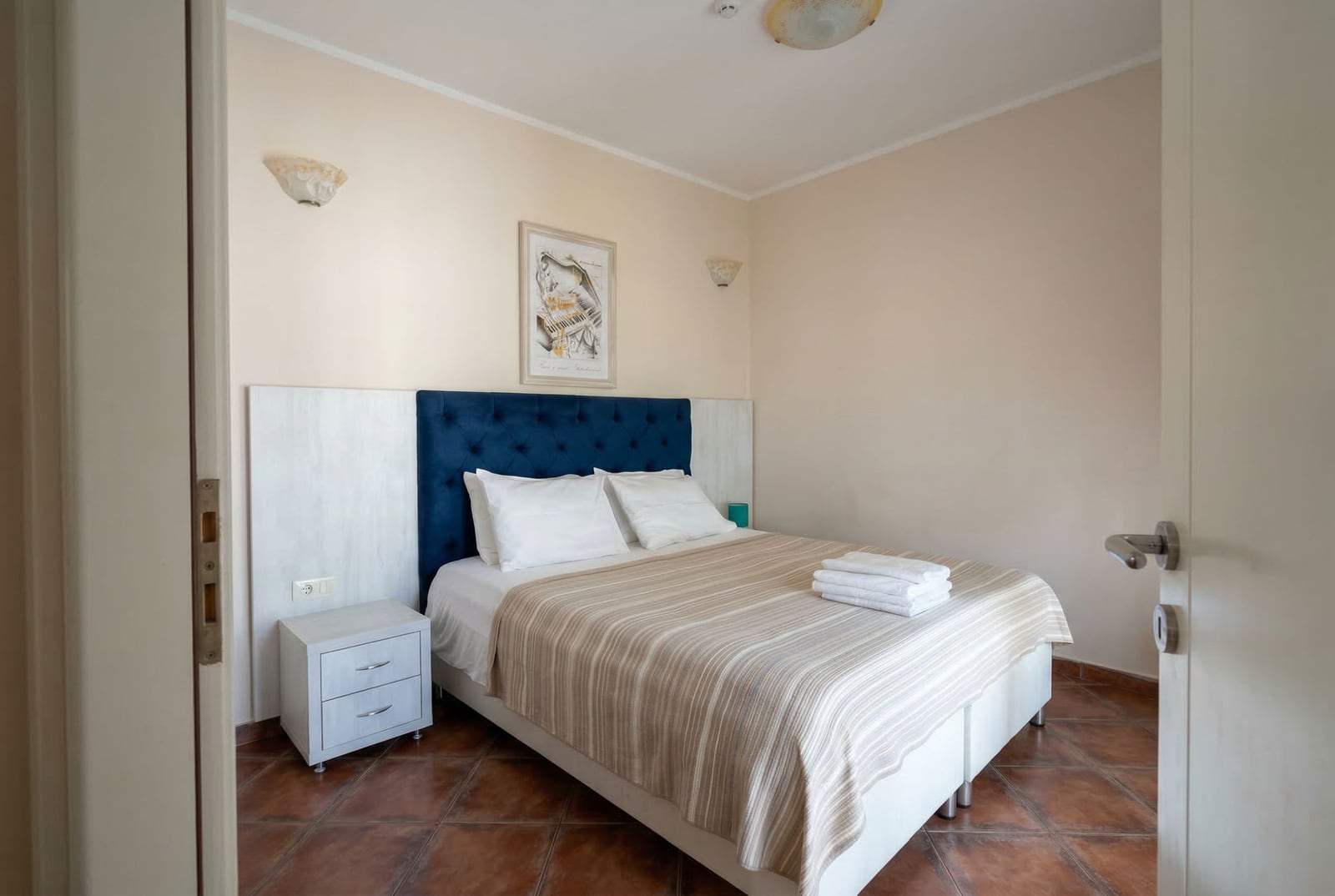 Ugodna spavaća soba sa bračnim krevetom i plavim uzglavljem u hotelu Bečići, Crna Gora. Svetao enterijer, pločice na podu.
