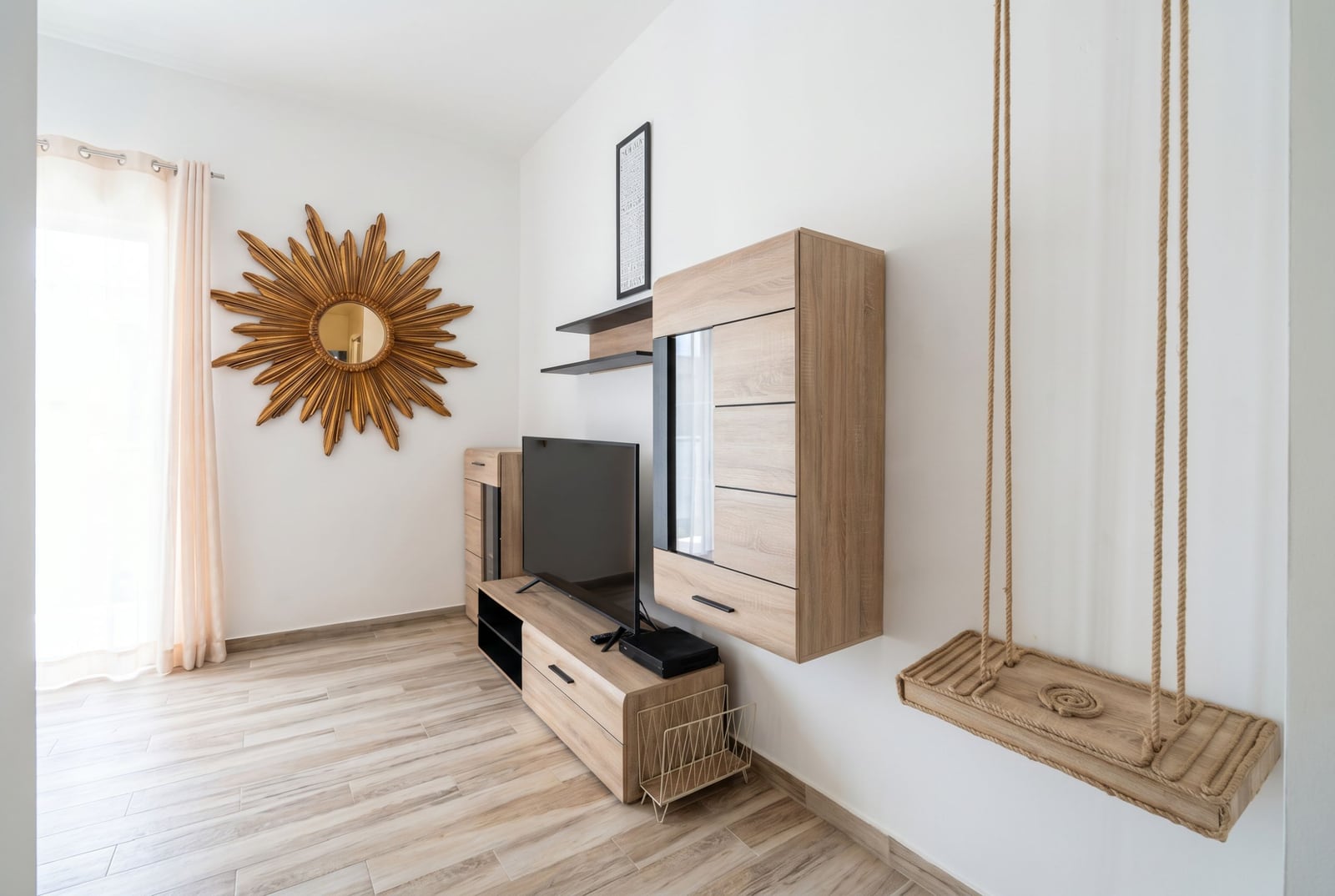 Wohnzimmer in einer Wohnung in Bečići, Montenegro: moderne Möbel in Holzoptik, TV-Bereich, dekorative Schaukel und Sonnenspiegel.