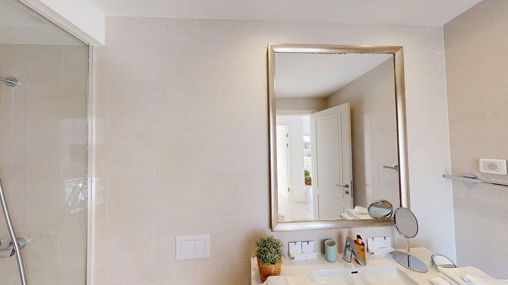Modernes Badezimmer mit Dusche und Spiegel in einer Wohnung, Luštica, Montenegro. Helle Fliesenverkleidung.