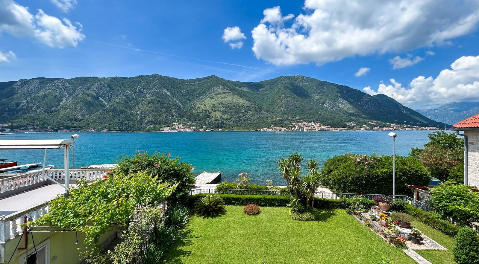 Blick auf die Bucht von Kotor und die Berge von der Terrasse der Villa in Dobrota, Montenegro: gepflegter Garten, viel Grün und direkter Zugang zum Meer.