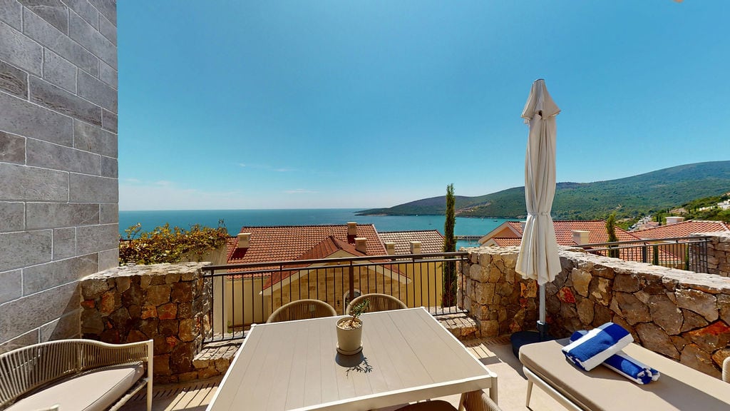 Terrasse mit Möbeln und Meerblick in der Wohnanlage Luštica, Montenegro: Steinverkleidung, Tisch und Liegestuhl.