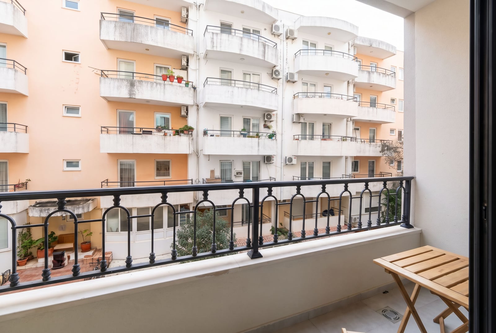 Balkon sa drvenim stolićem i kovanom ogradom sa pogledom na susedne stambene zgrade u Budvi, Crna Gora