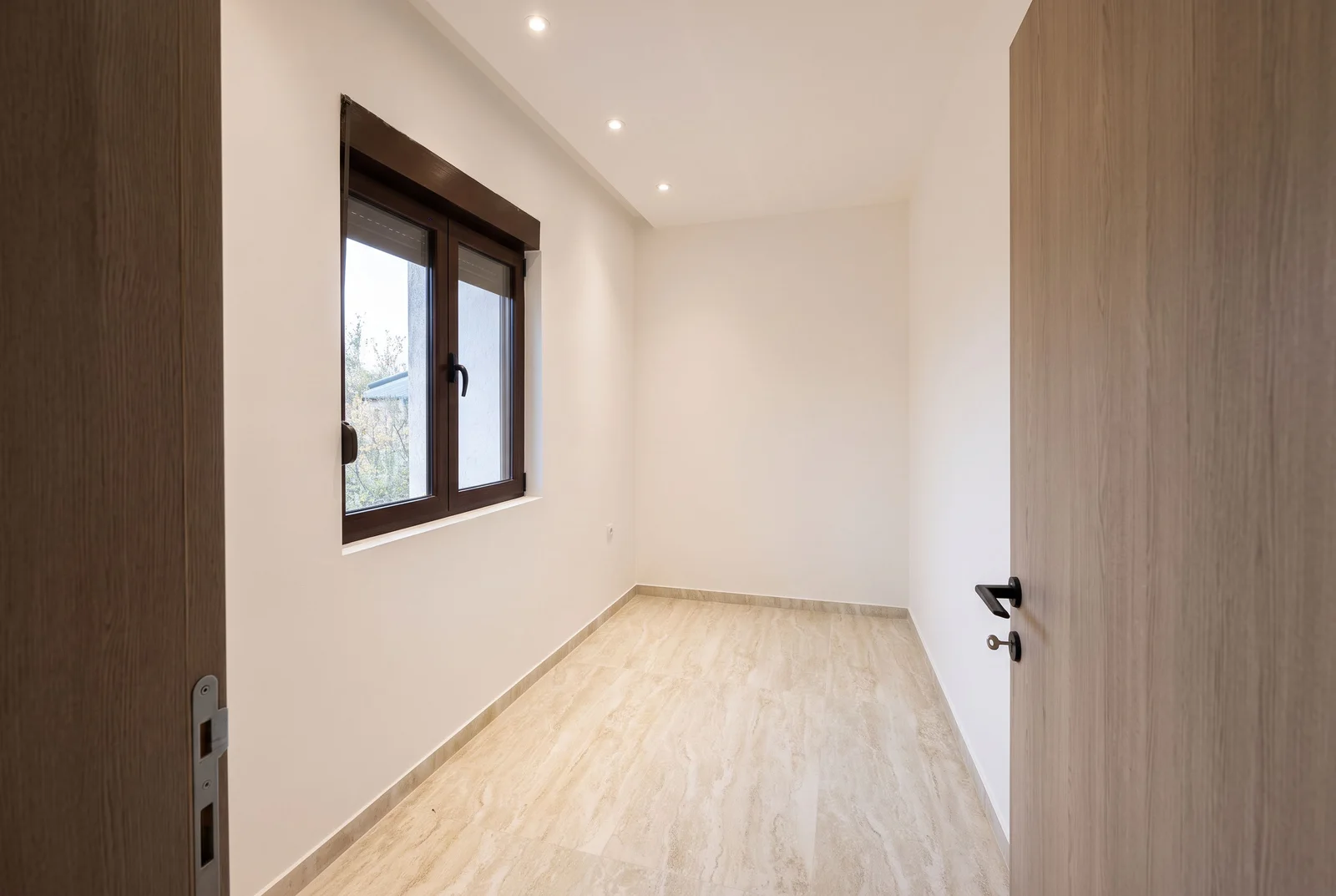 Empty room with light laminate flooring, white walls, a window, and a wooden door.