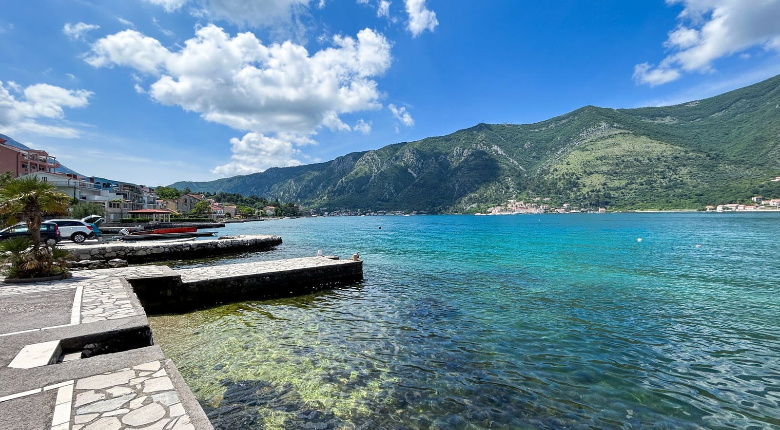 Blick auf das Meer und die Berge vom privaten Steg der Villa in Dobrota, Montenegro. Kristallklares Wasser und die Küstenlinie an einem sonnigen Tag.