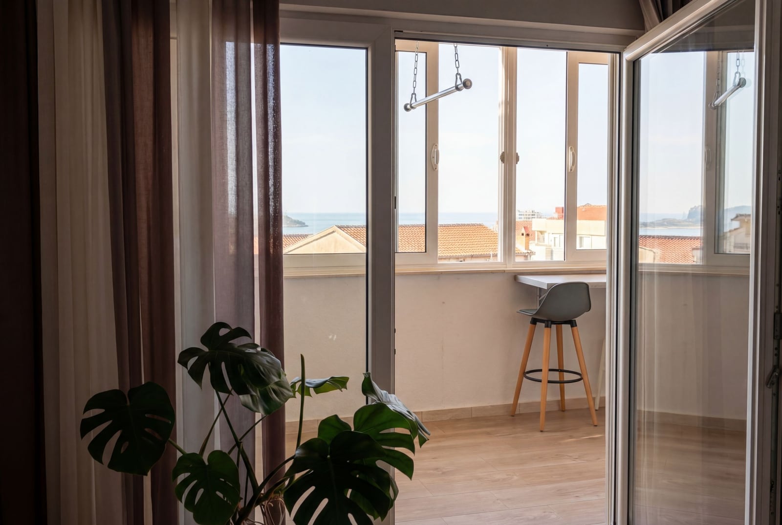 Balcony in an apartment in Budva, Montenegro: bar counter, chair, sea view and tiled roofs, panoramic glazing.