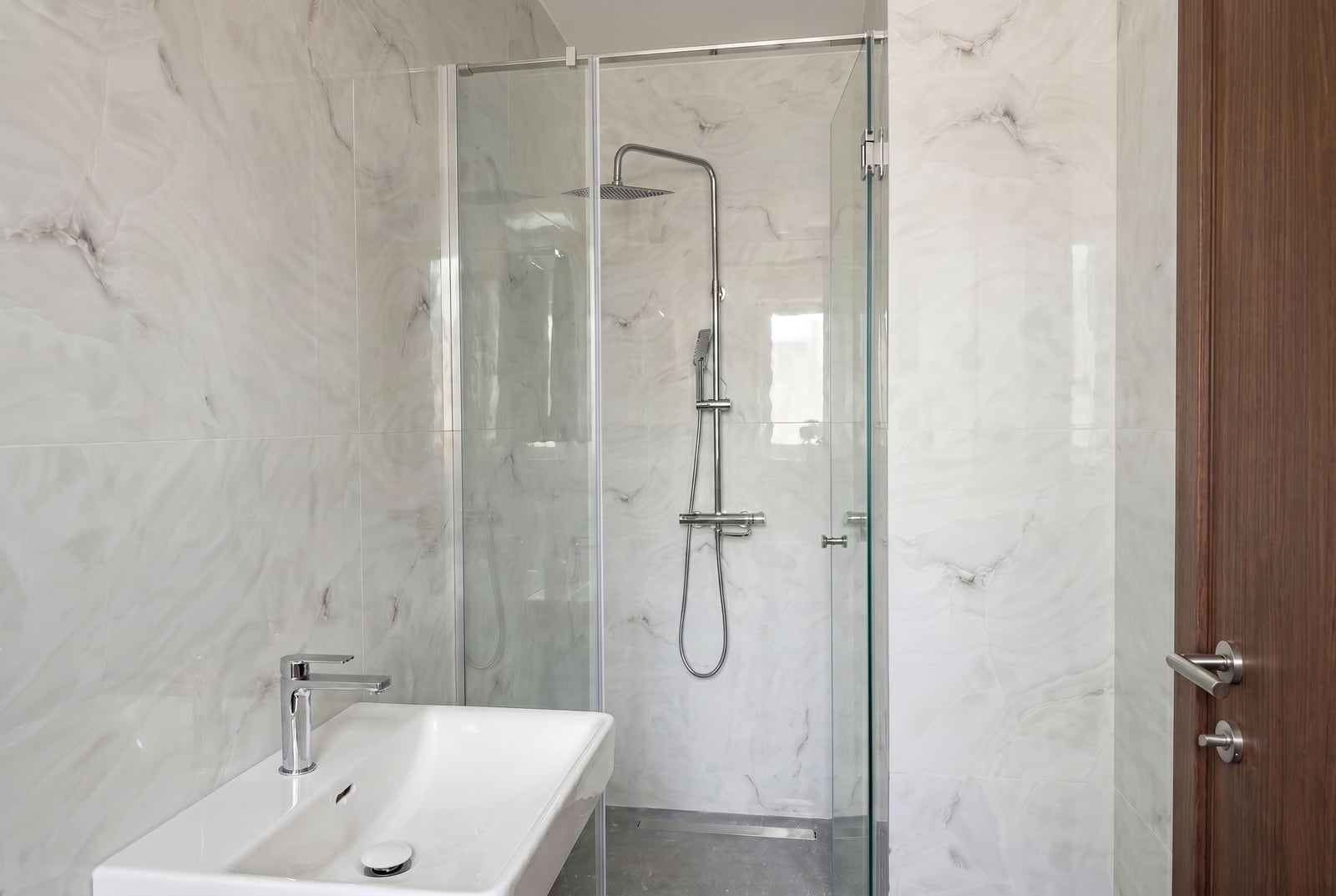 Budva, Karadağ'daki bir dairede modern banyo: duşakabin, mermer görünümlü açık renkli fayanslar ve sıhhi tesisat.