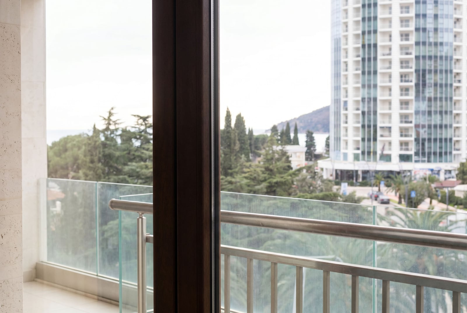View from the apartment balcony in Budva, Montenegro: glass railing, city panorama, greenery, and a modern residential complex.