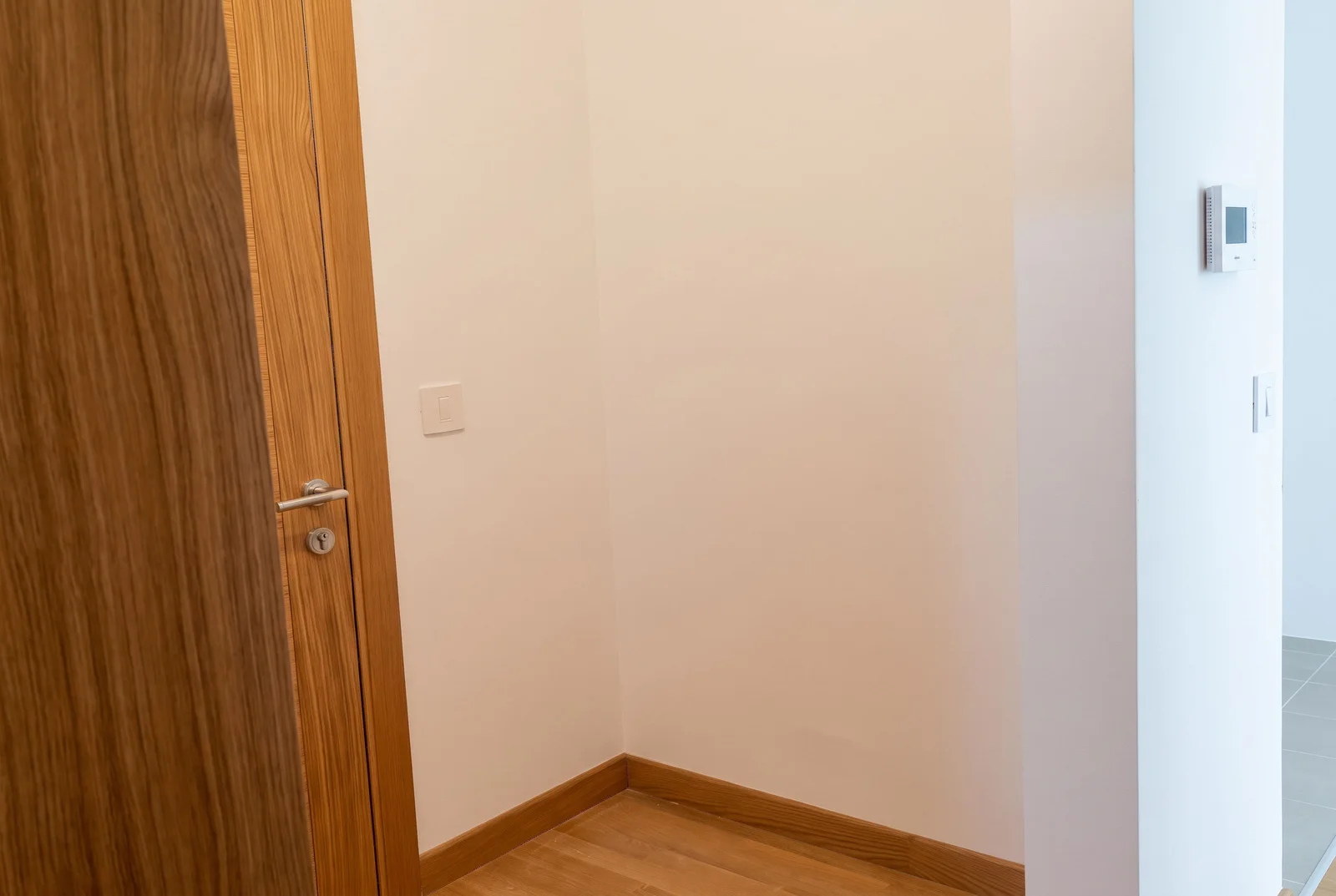Pran ugao sa drvenim vratima, svetlim zidovima, laminatom i termostatom na zidu.