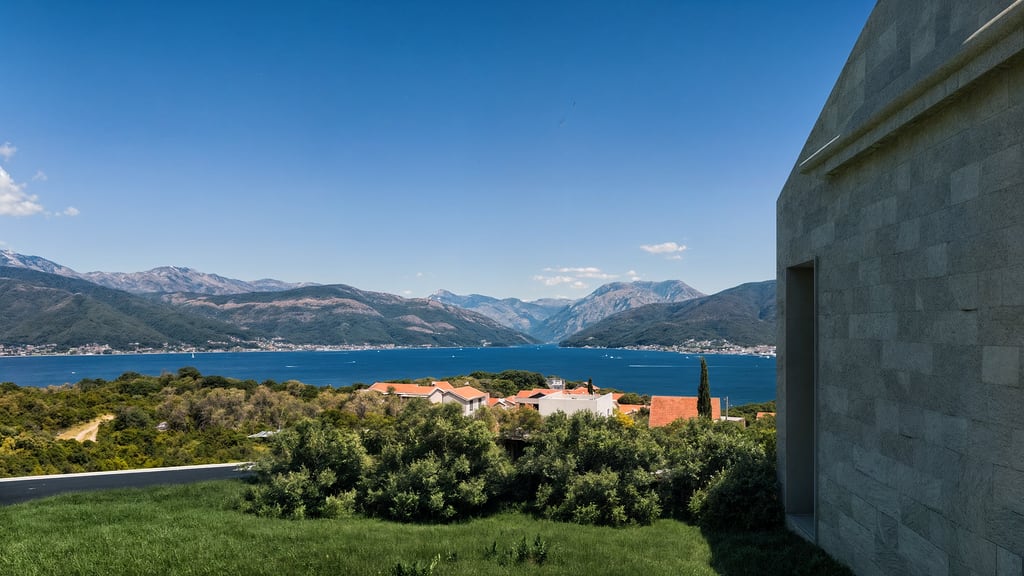 Panoramablick auf die Bucht von Kotor und die Berge von einer modernen Villa in Luštica, Montenegro, mit Steinverkleidung des Gebäudes.