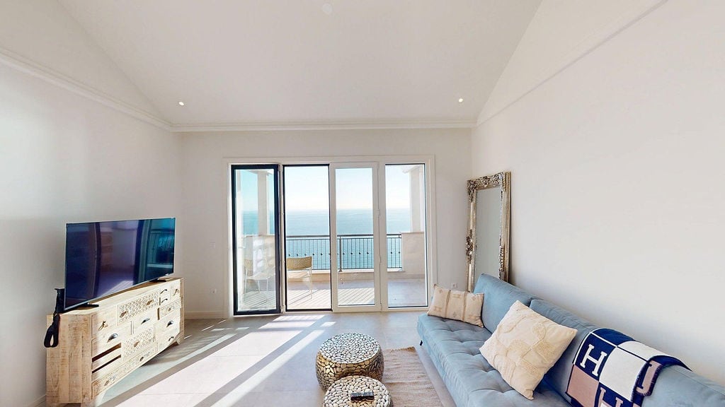 Helles Wohnzimmer mit Meerblick in der Apartmentanlage Luštica Bay, Montenegro: weiches Sofa, TV-Bereich und Zugang zur Terrasse.