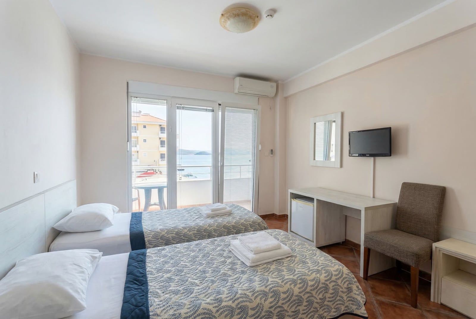 Spavaća soba u hotelu Bečići, Crna Gora: dva kreveta, radni sto, TV i izlaz na balkon s pogledom na more.