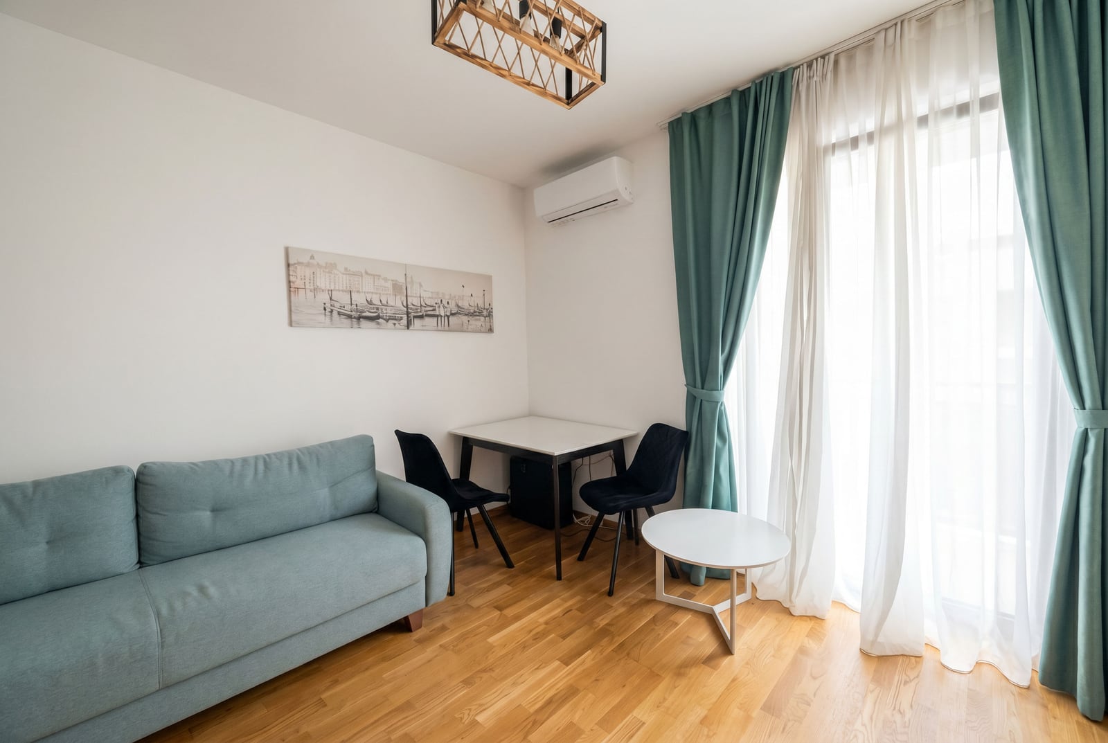 Wohnzimmer in einem Apartment in Bečići, Montenegro: Sofa, Essbereich, Parkettboden und Panoramafenster mit türkisfarbenen Vorhängen.