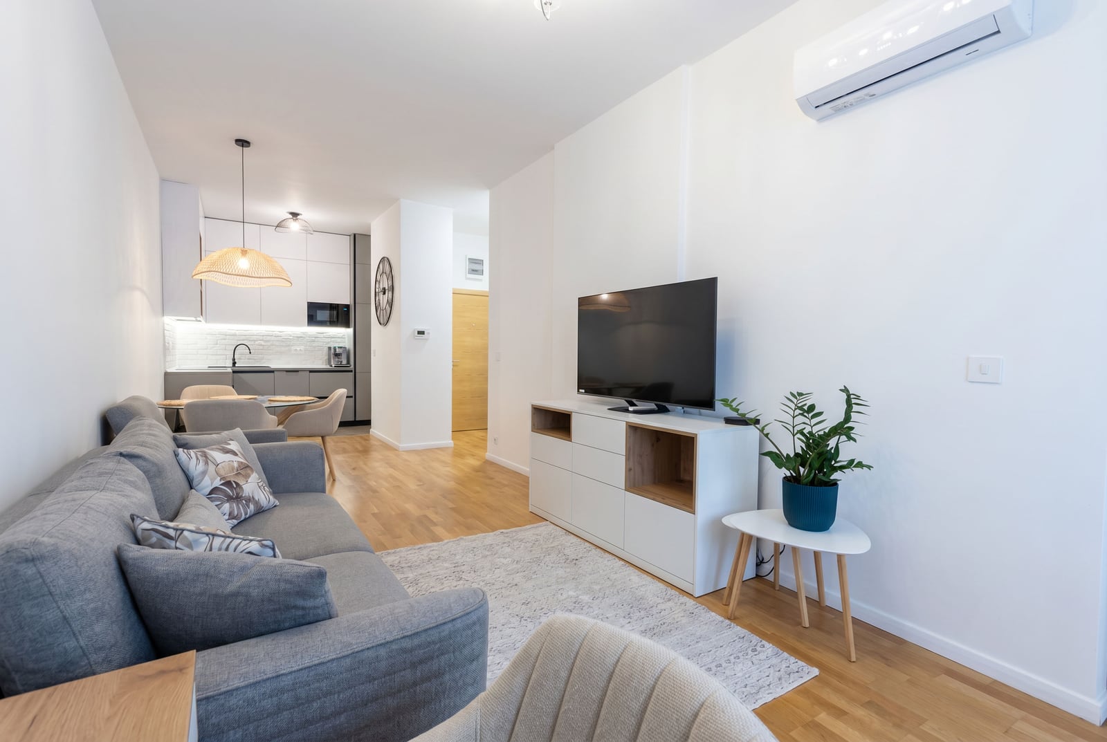 Moderan dnevni boravak sa kuhinjom u stanu u Bečićima, Crna Gora: siva sofa, TV zona, svetao enterijer i parket.