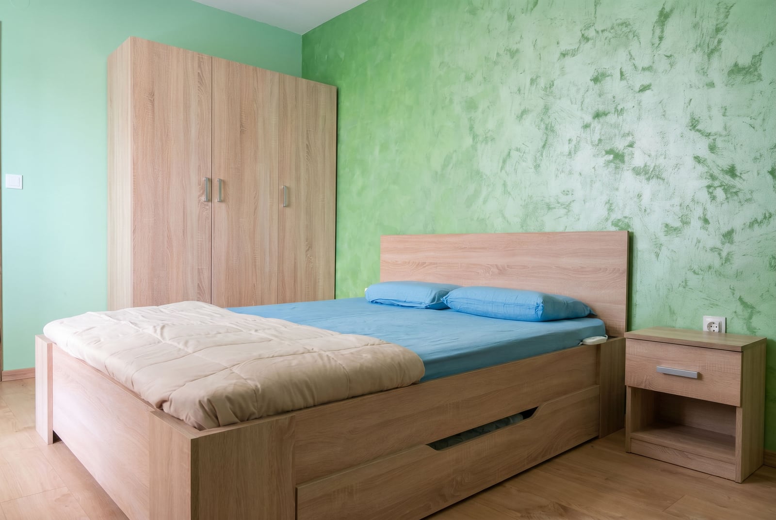 Bedroom in a Budva apartment, Montenegro: double bed, light wood wardrobe and bedside table, green walls.