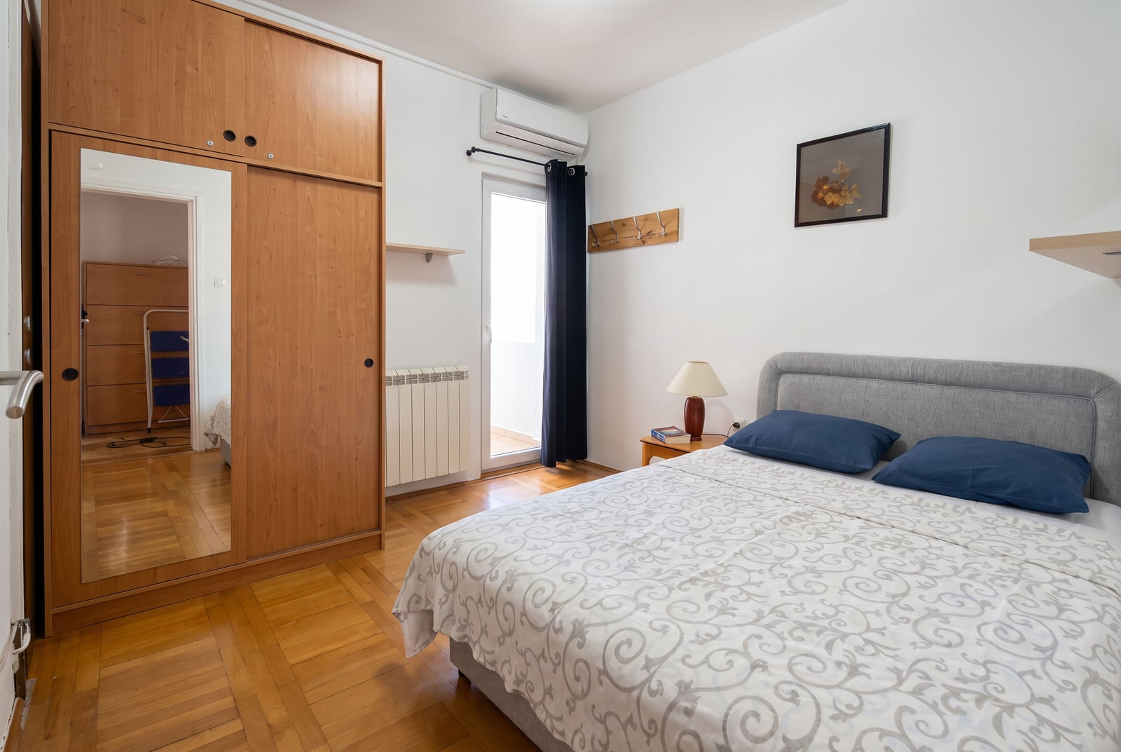 Spavaća soba sa bračnim krevetom, drvenim ormanom sa ogledalom i izlazom na balkon u stanu u Budvi, Crna Gora