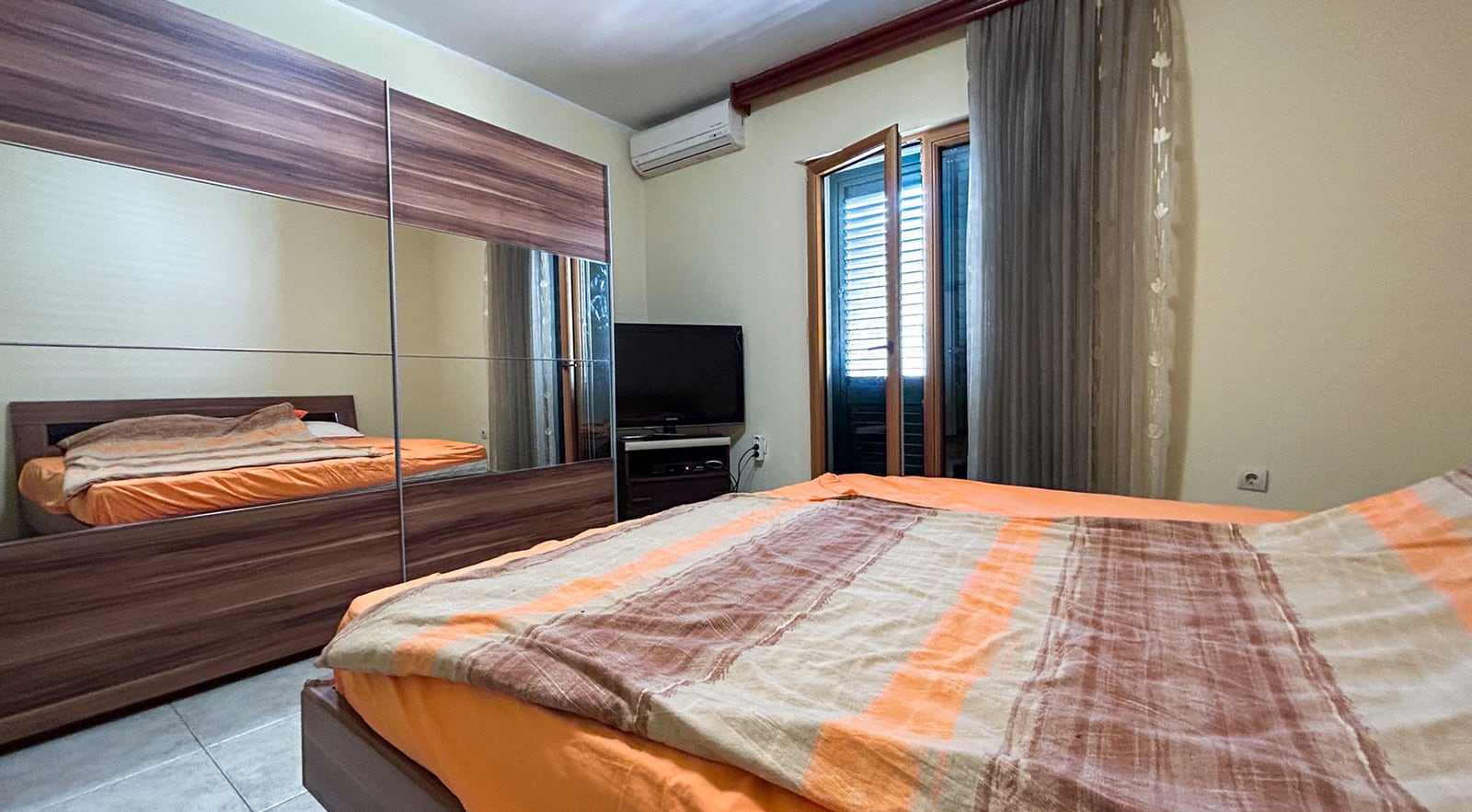 Schlafzimmer in einer Villa in Dobrota, Montenegro: Doppelbett, Spiegel-Schiebetürschrank, Fernseher und Zugang zum Balkon.