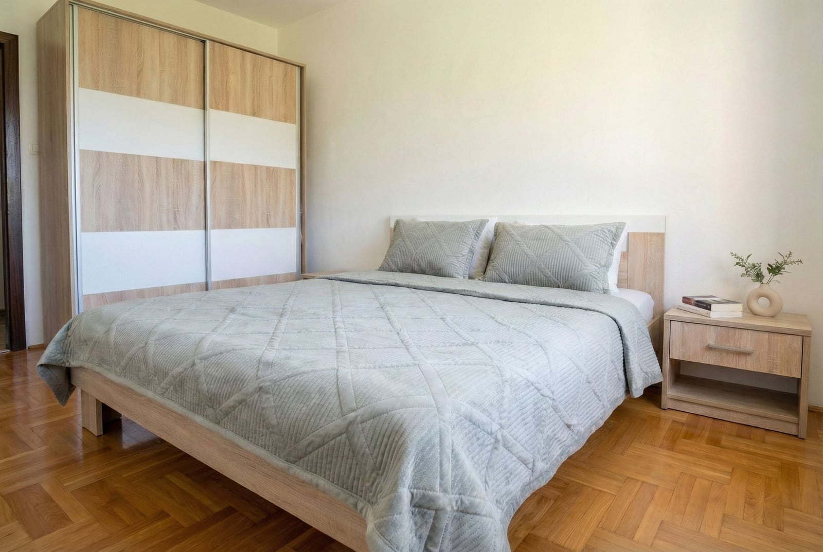 Svetla spavaća soba u stanu u Budvi, Crna Gora: bračni krevet, ugradni ormar i parketni pod u modernom stilu.