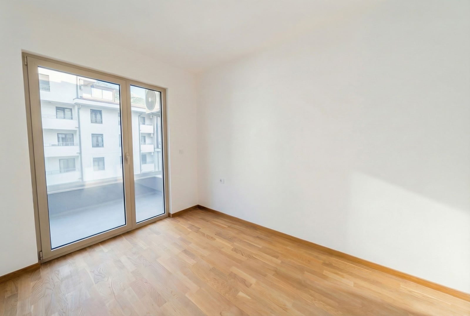 Svetla spavaća soba sa parketom i izlazom na balkon u stanu, grad Bečići, Crna Gora.