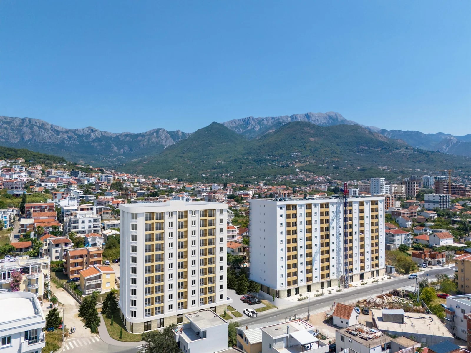 Luftaufnahme moderner Wohnanlagen in Bar, Montenegro, vor malerischer Bergkulisse.
