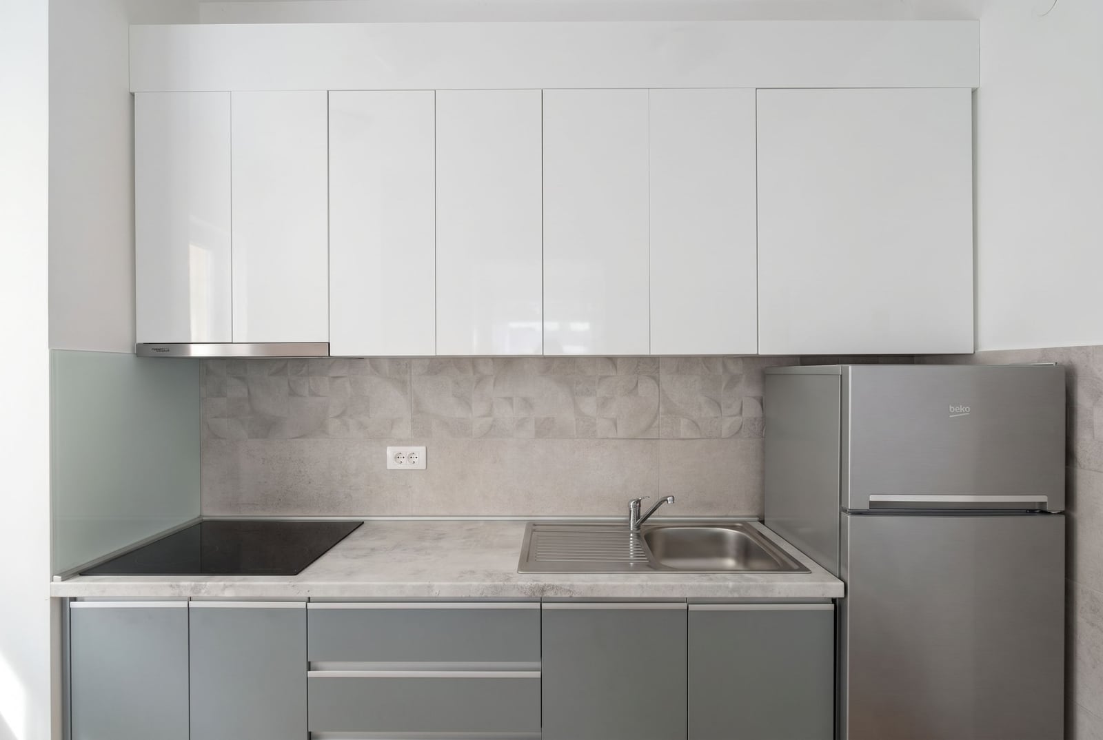 Modern kitchen in an apartment in Budva, Montenegro: white glossy cabinets, built-in appliances, and a gray backsplash.