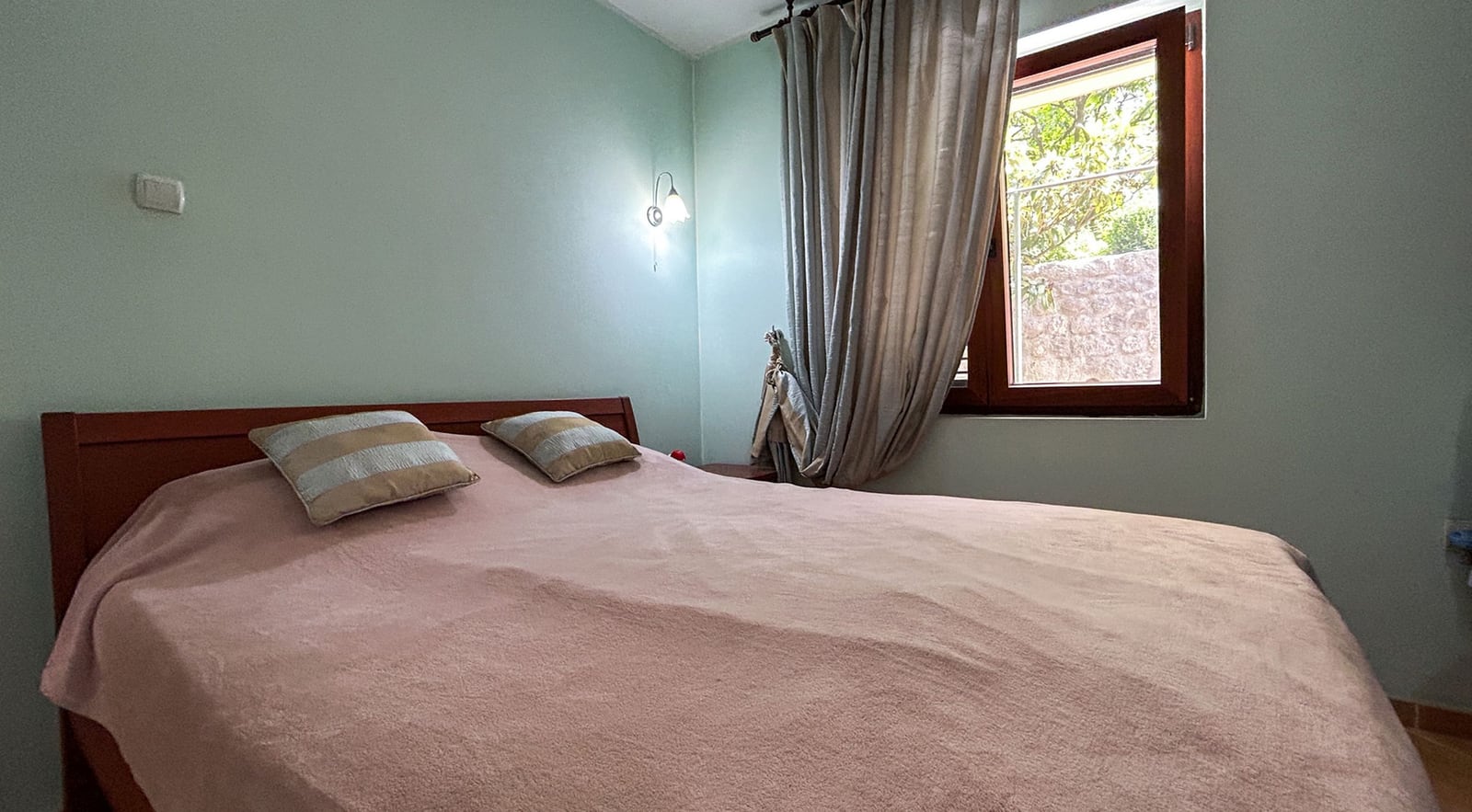 Gemütliches Schlafzimmer mit Doppelbett in einer Villa in Dobrota, Montenegro: helle Wände, Holzmöbel und Blick aus dem Fenster.
