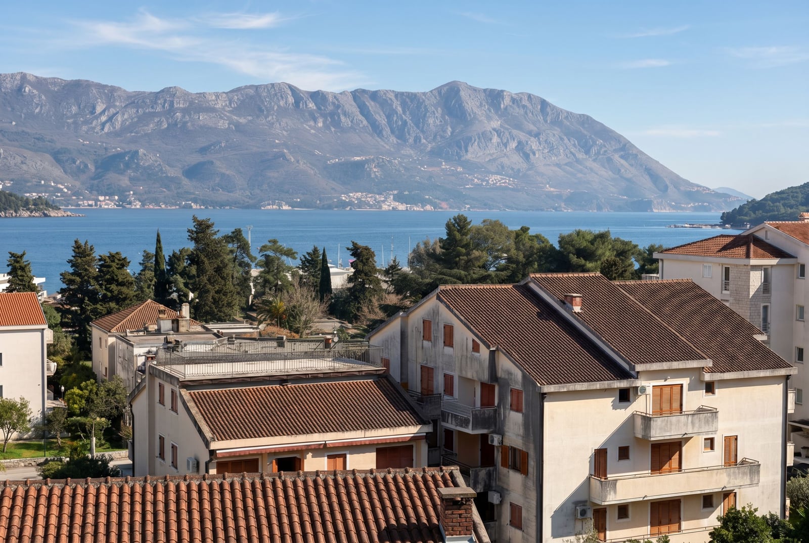 Panoramski pogled na more i planine iz stana u Budvi, Crna Gora: stambeni deo sa krovovima od crepa i zelenilom.