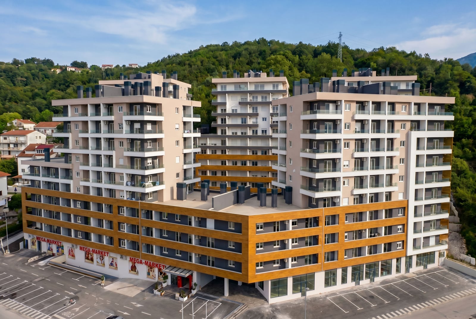 Moderan stambeni kompleks sa supermarketom u Budvi, Crna Gora: pogled na višespratnicu sa balkonima i parkingom.