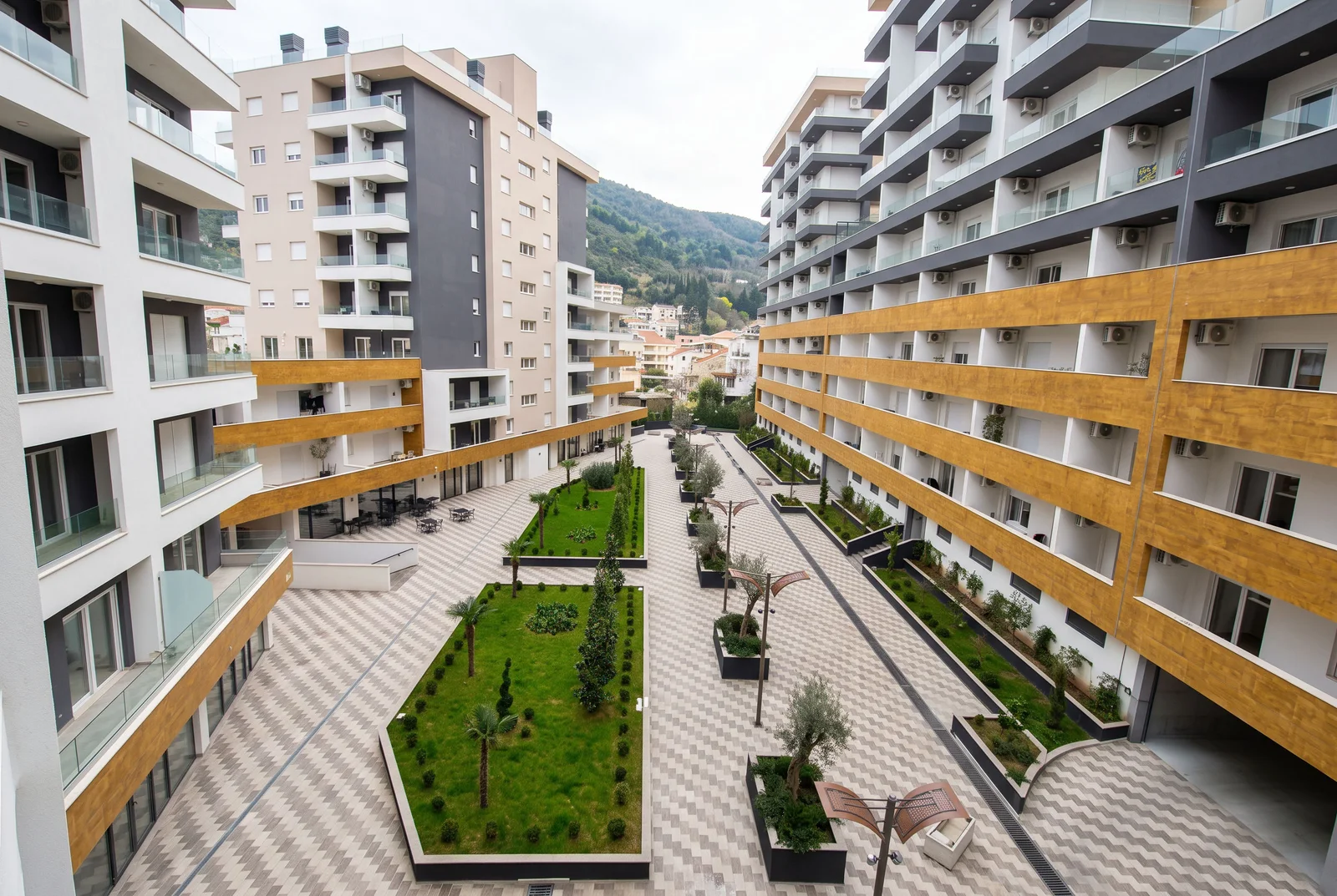 View of a residential complex courtyard featuring lawns, paved walkways, and multi-story buildings.