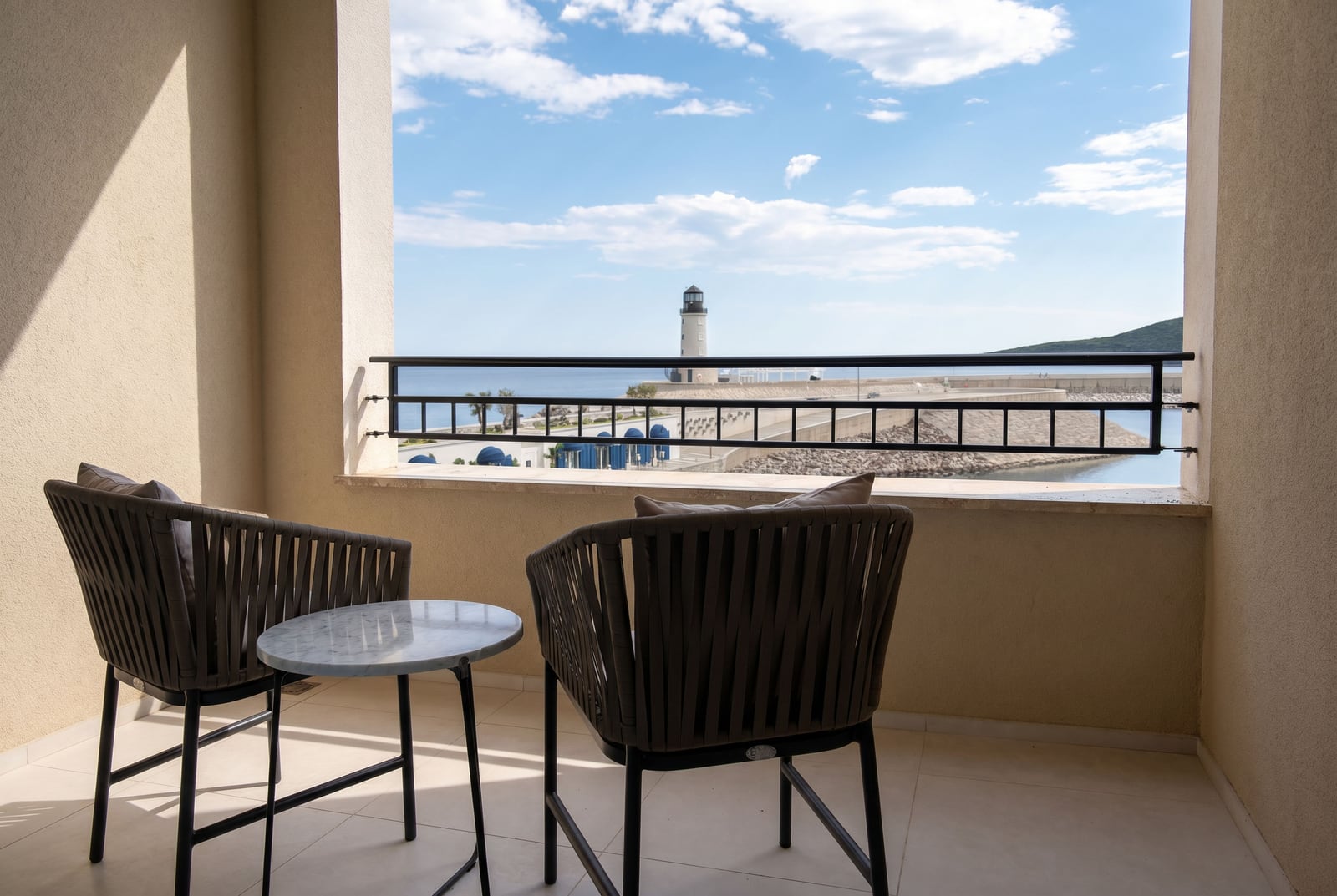 Balkon mit Korbmöbeln und Blick auf den Leuchtturm und das Meer in Luštica Bay, Montenegro. Modernes Apartment-Interieur.