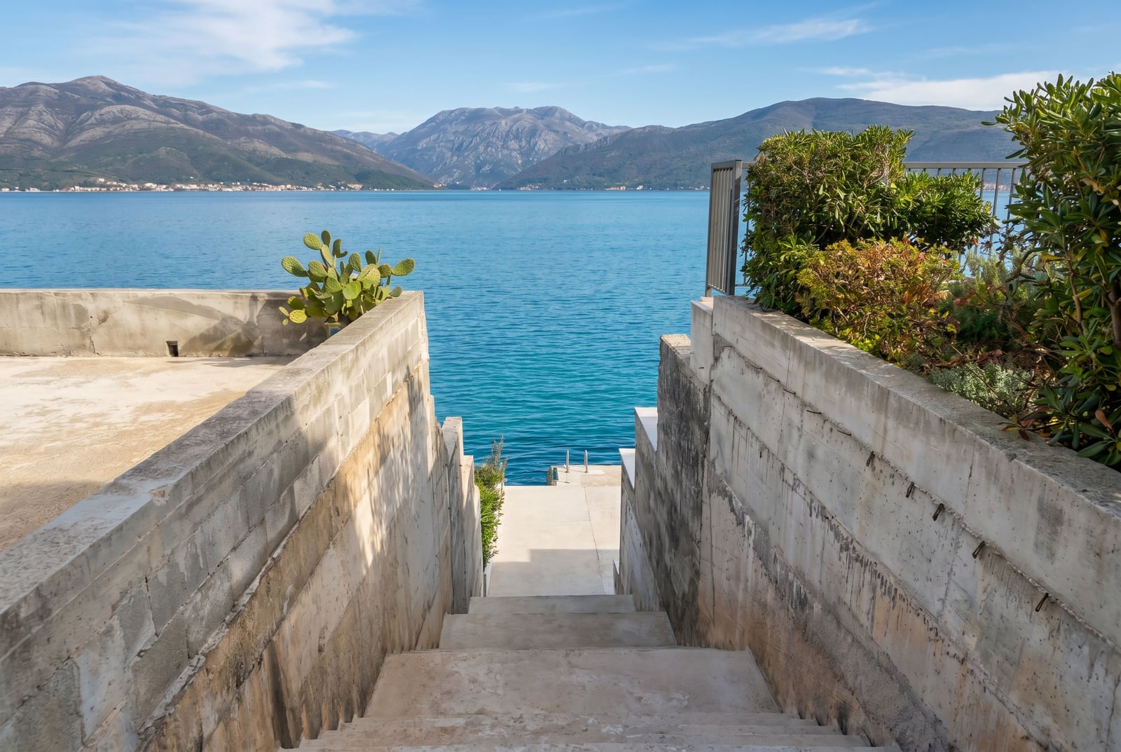 Escalier en béton menant à la mer et ponton privé devant une maison à Krašići, Monténégro, avec vue panoramique sur la baie de Kotor.