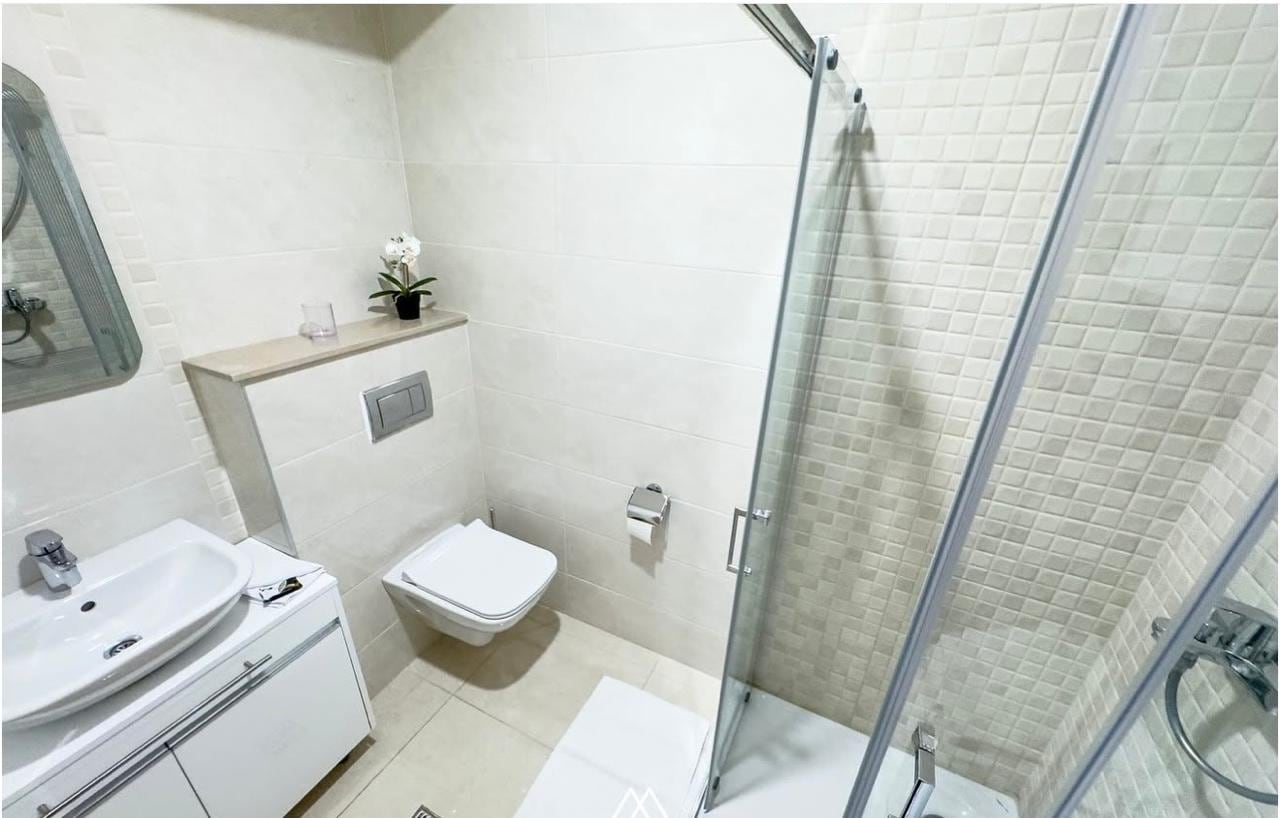 Modern bathroom with a walk-in shower in an apartment in Becici, Montenegro: light-colored tiles and fixtures.