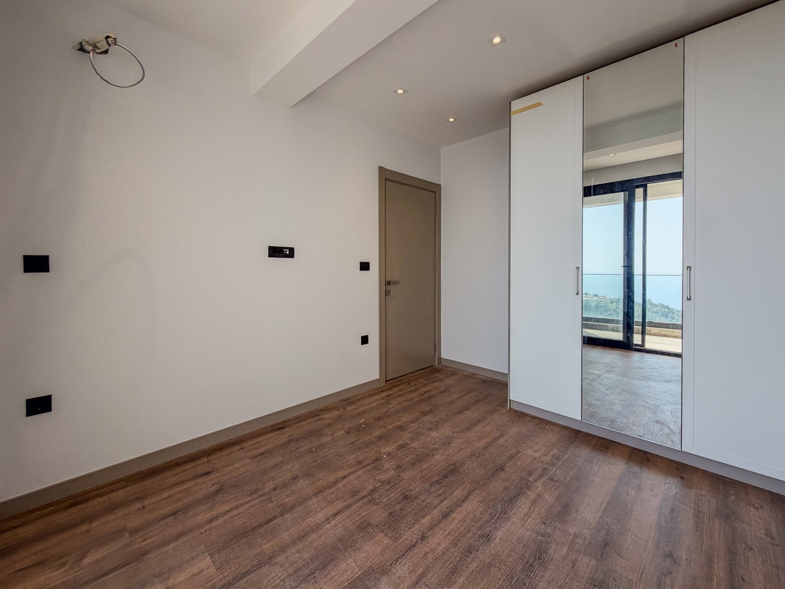 Bright bedroom with white walls, a mirrored wardrobe, and a sea view in an apartment in Budva, Montenegro