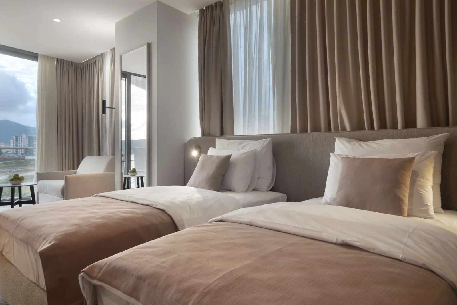 Moderna spavaća soba sa dva kreveta, panoramskim prozorom i pogledom na planine u hotelu u Crnoj Gori, Bečići