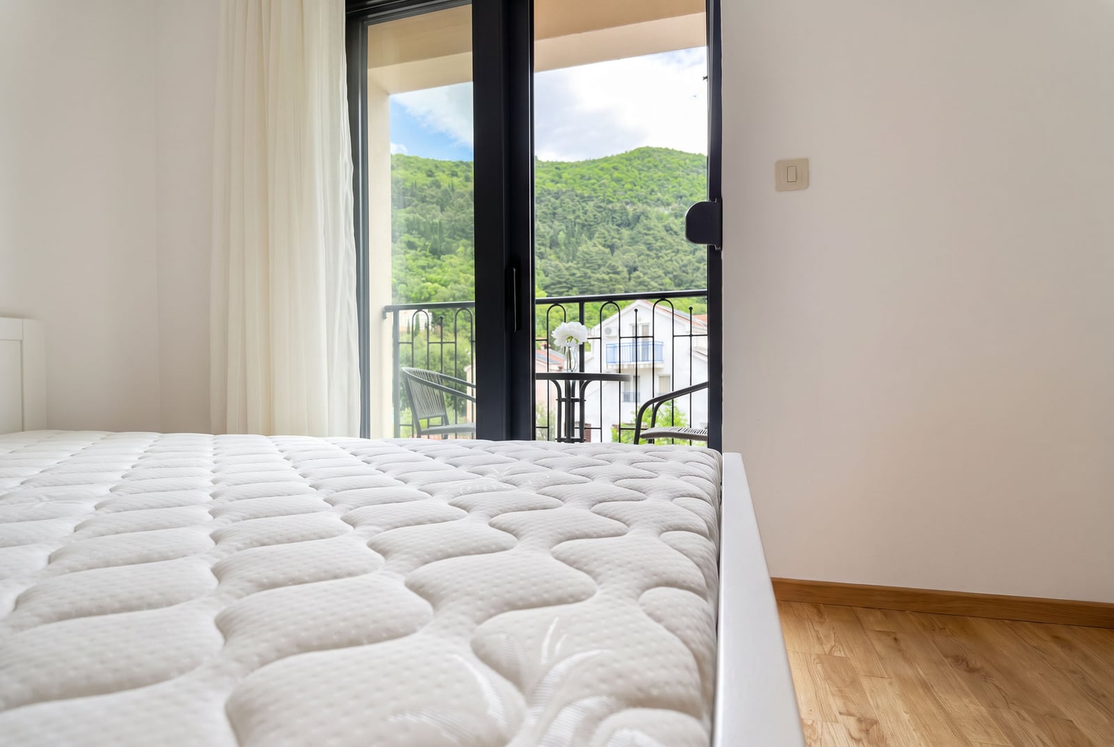 Bedroom with a white bed and panoramic balcony access with mountain views in an apartment in Budva, Montenegro