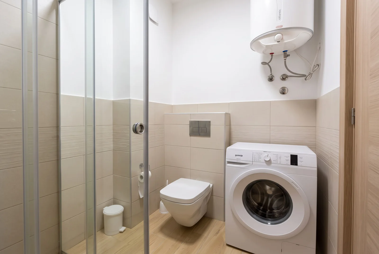 Bathroom featuring a glass shower, wall-mounted toilet, washing machine, and overhead water heater.