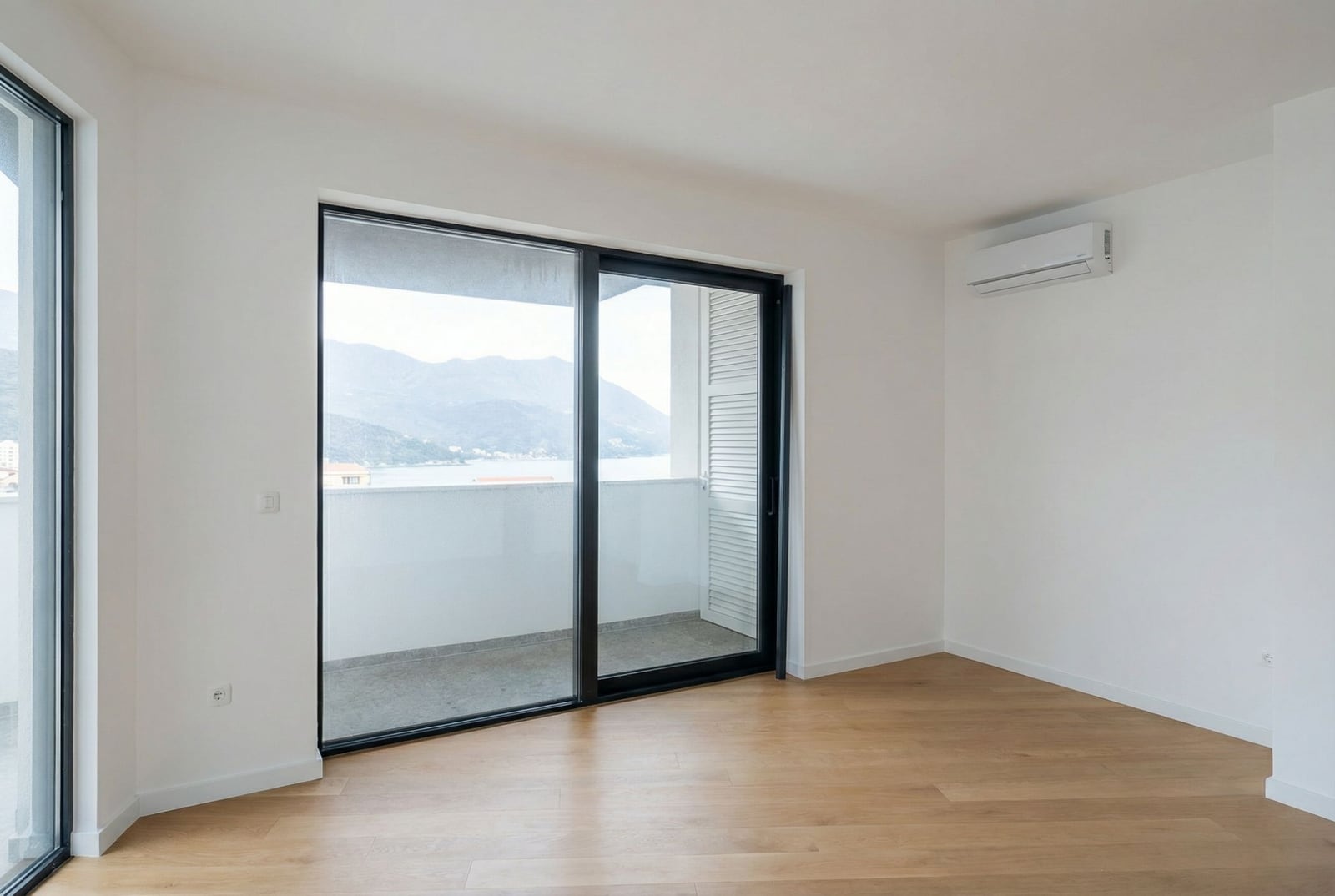 Svetao dnevni boravak u stanu u Bečićima, Crna Gora, sa panoramskim izlazom na balkon i pogledom na more i planine.