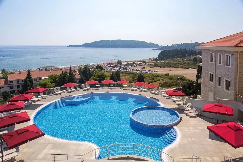 Outdoor swimming pool with red umbrellas and a sea view at a residential complex, Becici, Montenegro.