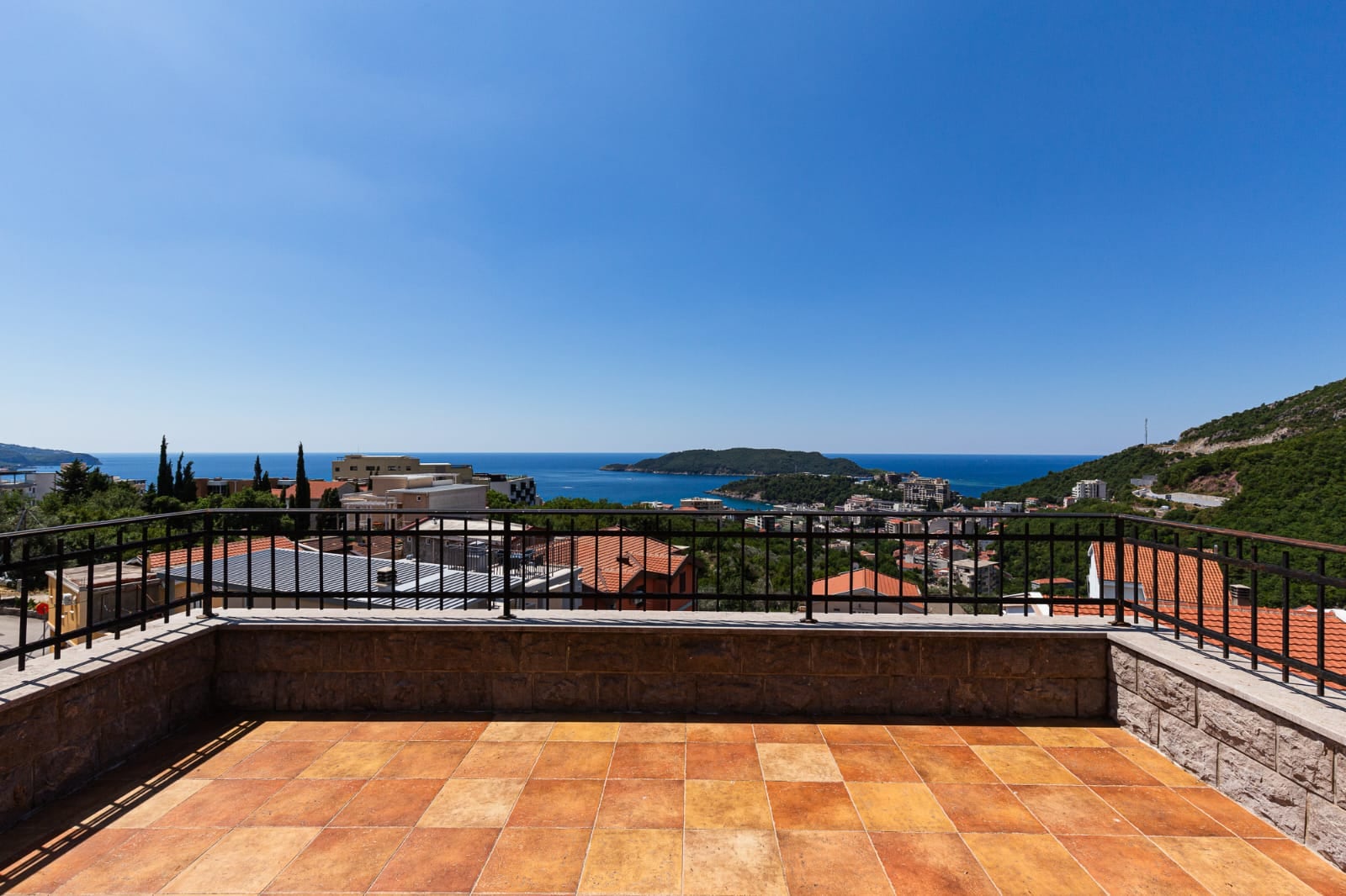 Terrasse spacieuse d'une villa à Bečići, au Monténégro, offrant une vue panoramique sur la mer, les montagnes et les toits en tuiles de la ville.