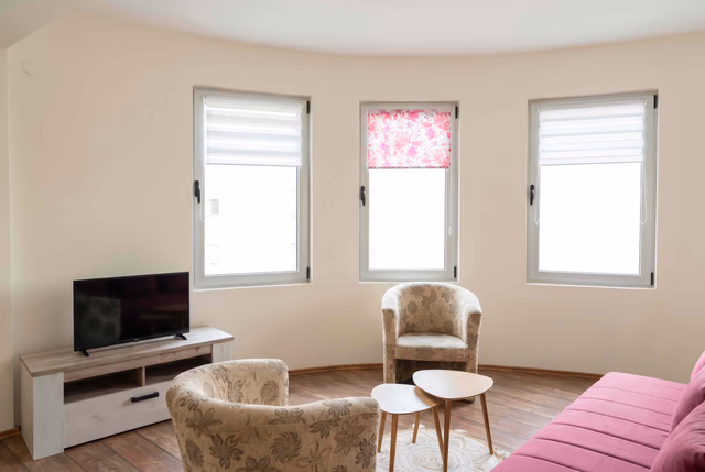 Helles Wohnzimmer mit Panoramafenstern in einer Wohnung in Bečići, Montenegro: Sessel, Sofa und TV-Bereich.
