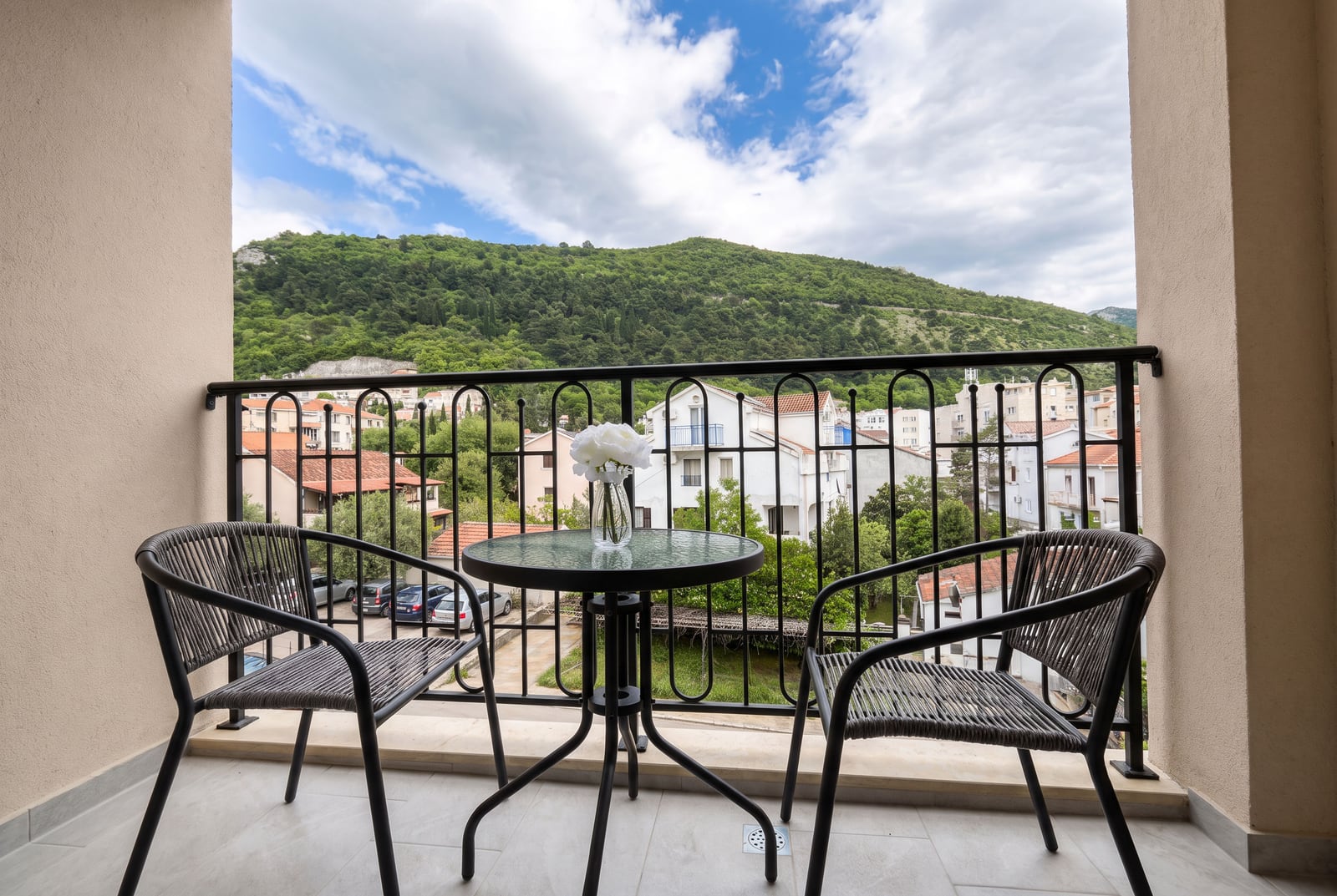 Balcony with wicker furniture and views of the mountains and city in an apartment in Budva, Montenegro