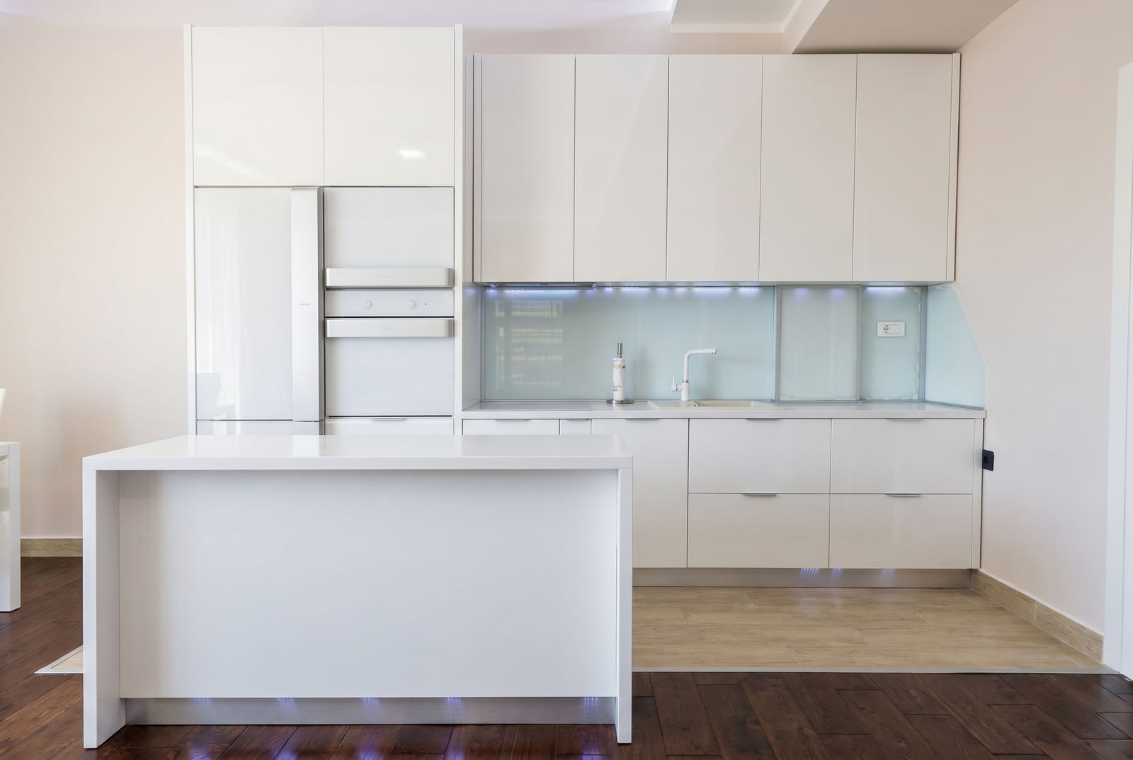 Modern white kitchen with an island and built-in appliances in an apartment in Budva, Montenegro. Interior with ambient lighting.
