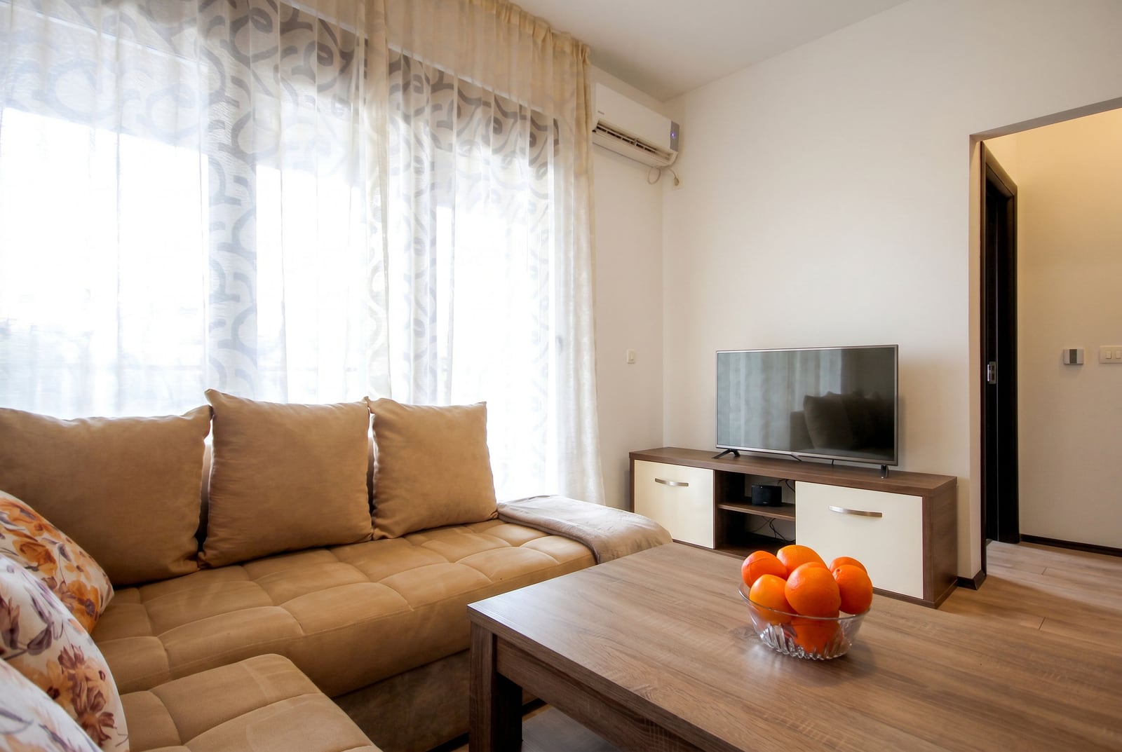Cozy living room with a beige sofa, TV area, and air conditioning in an apartment in Budva, Montenegro.