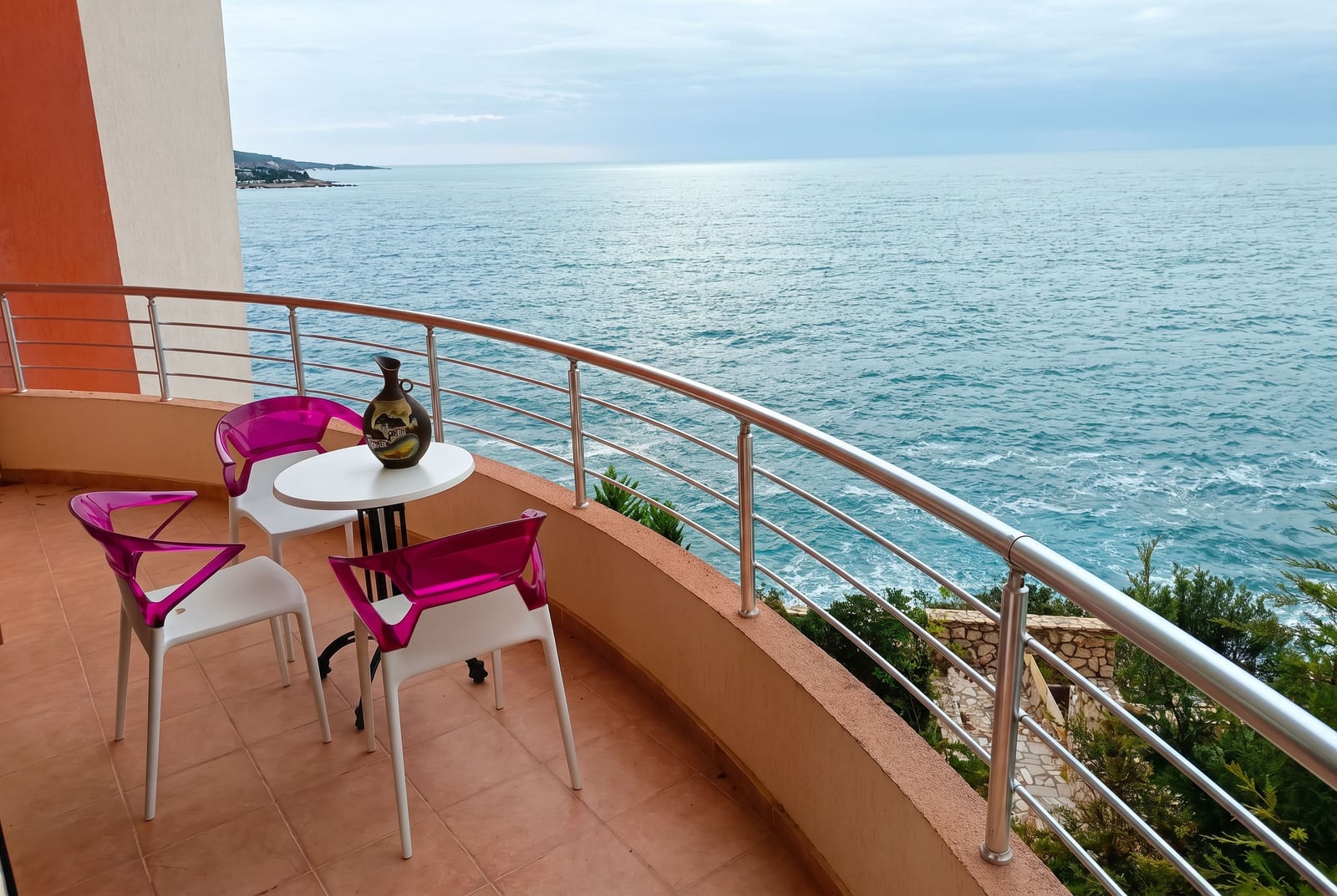 Balkon sa pogledom na more u stanu, grad Bar, Crna Gora: sto i roze stolice na terasi sa panoramskim pogledom.