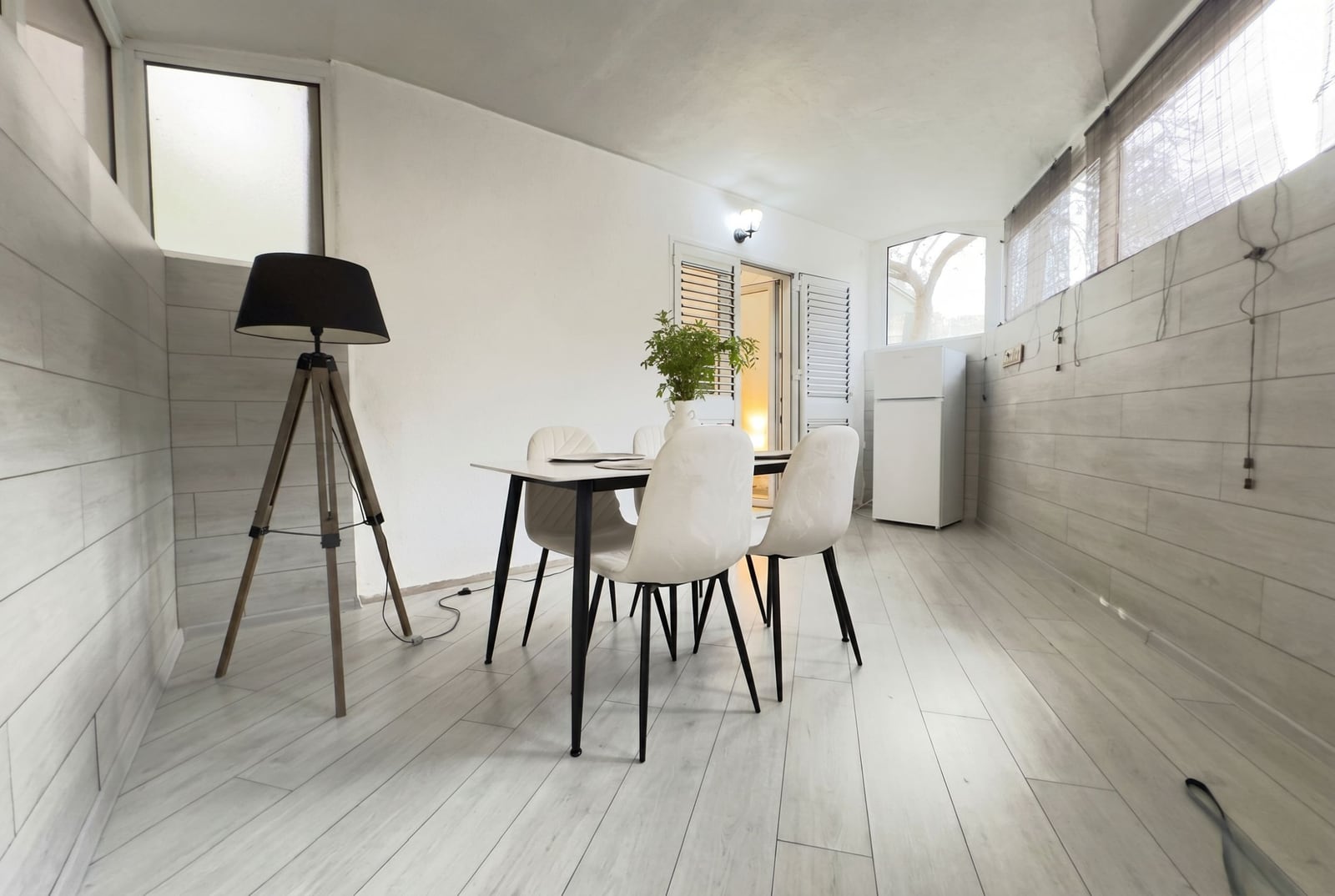 Bright dining area in an apartment in Budva, Montenegro: modern furniture, wood-style finishes, and a tripod floor lamp.