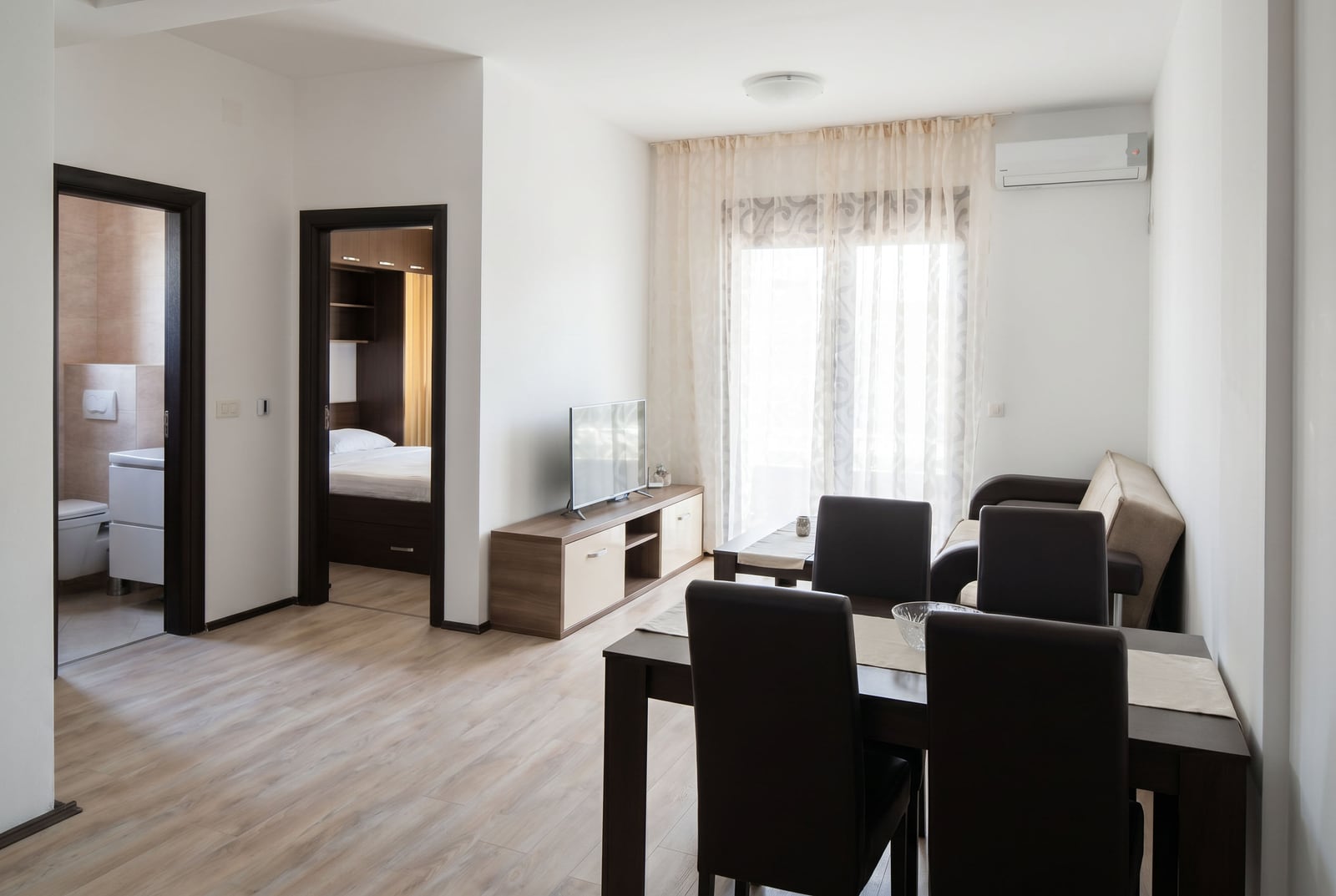 Living room with dining area in a Budva apartment, Montenegro: modern furniture, bright interior, and a view into the bedroom.