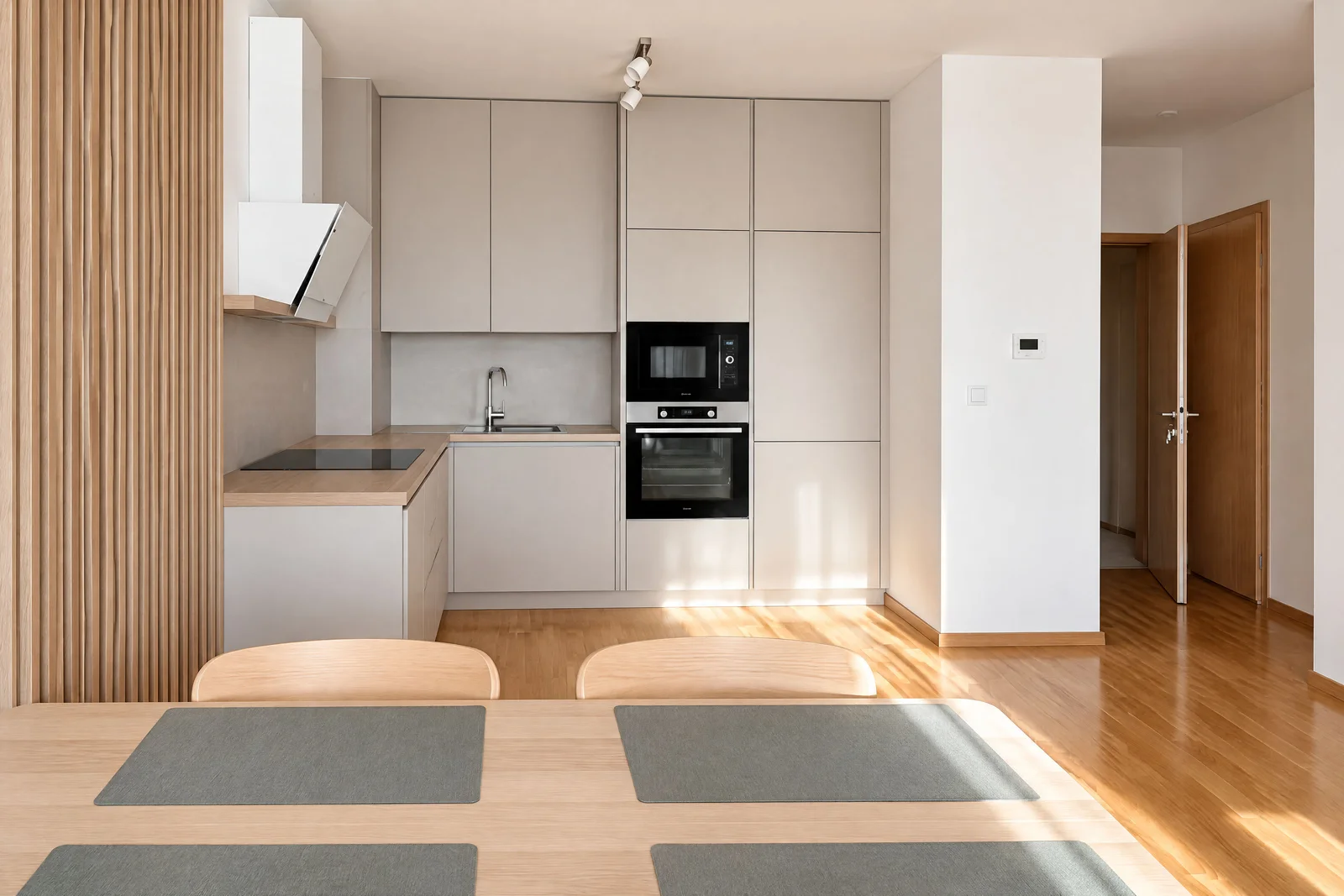 Açık renk dolapları, yerleşik fırın, mikrodalga, lavabo ve ön planda ahşap yemek masası olan modern mutfak.