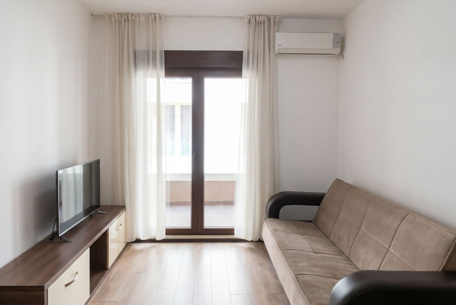 Bright living room with a sofa, TV stand, and balcony access in an apartment in Budva, Montenegro. Modern interior.