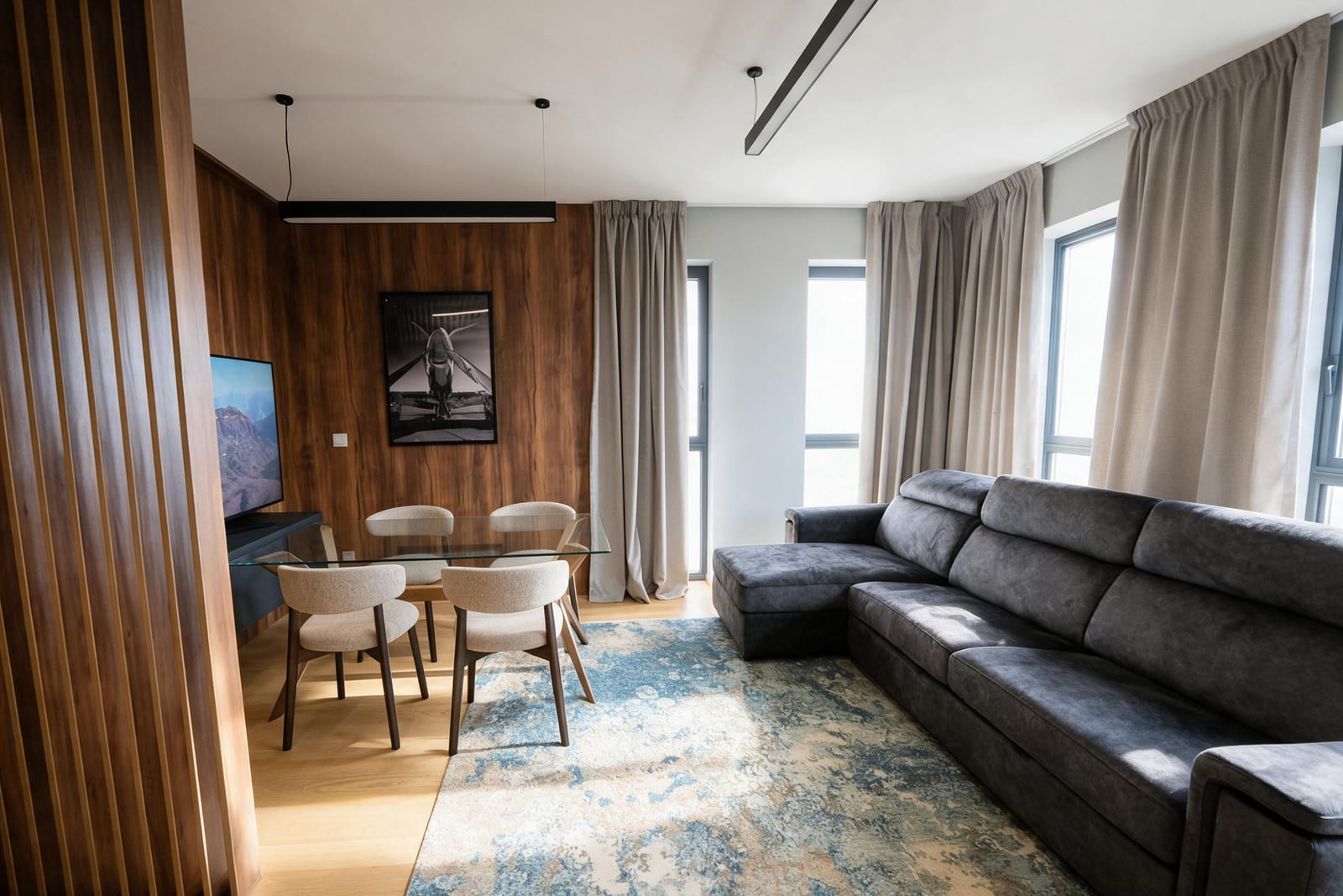 Modern living room with a soft gray sofa, dining area, and wooden wall paneling in an apartment in Budva, Montenegro.