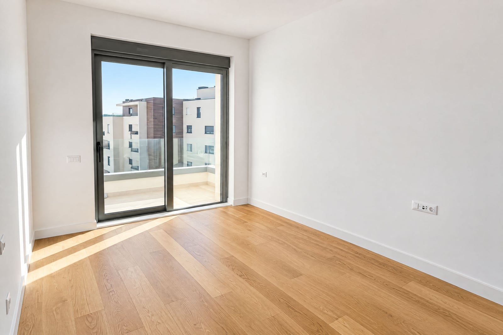 Bright empty bedroom with parquet flooring and a panoramic window to the terrace in a new building in Becici, Montenegro